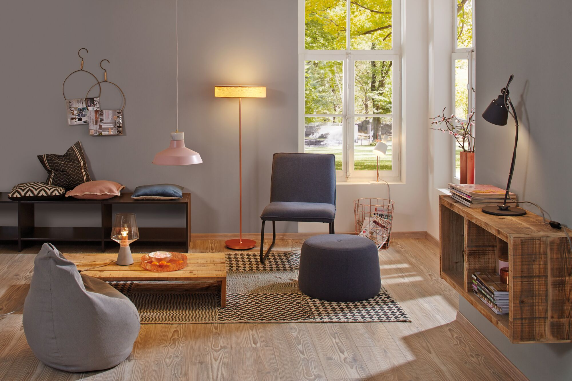Ein Wohnzimmer mit Sitzmöbeln, Lampen und einem Holztisch. Draußen grüne Bäume.