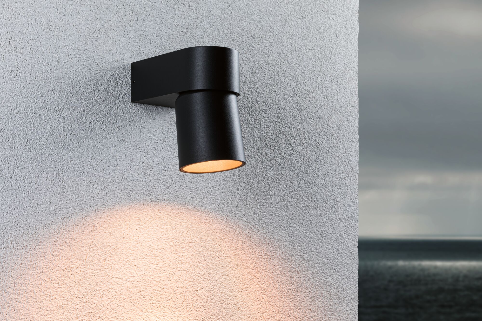 Czarny reflektor ścienny oświetla białą ścianę. Morze i niebo w tle.