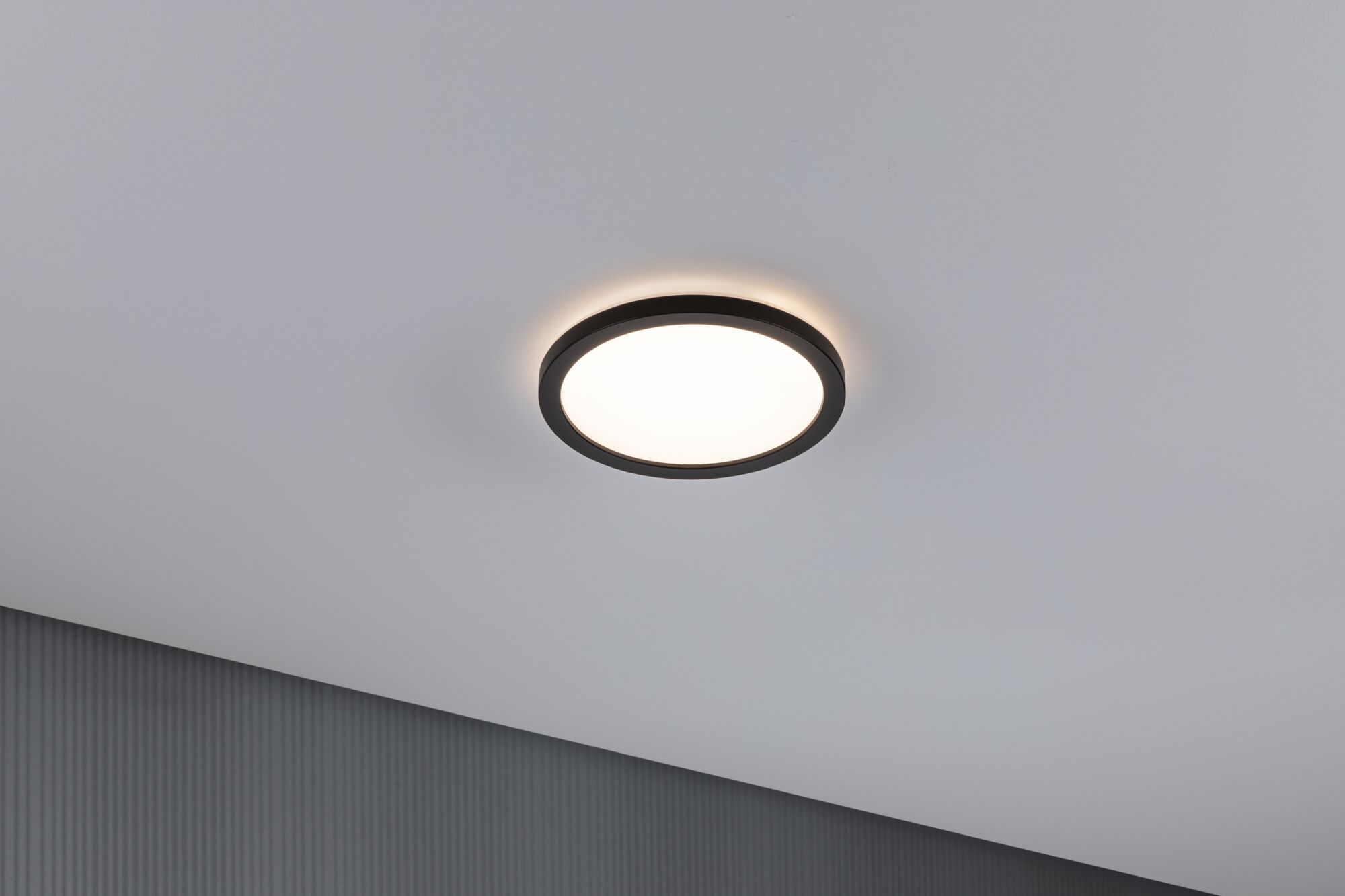 Un plafonnier rond avec cadre noir éclaire un plafond blanc.