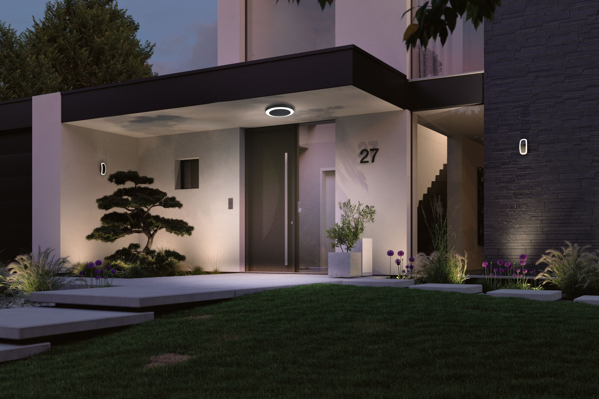 Moderne Villa bei Nacht mit beleuchtetem Eingang, Bonsai und Ziergräsern.