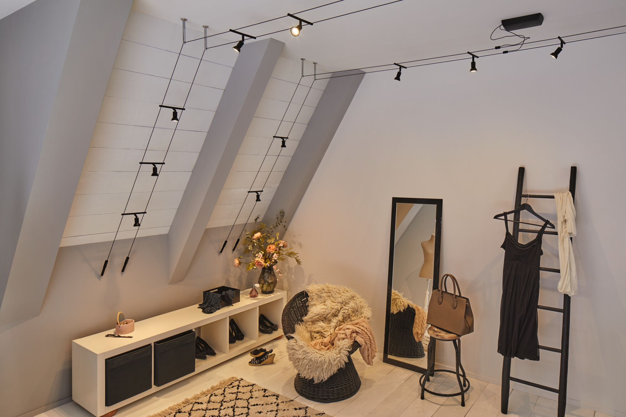 Un dressing avec plafonds mansardés et plusieurs lumières sur câbles.
