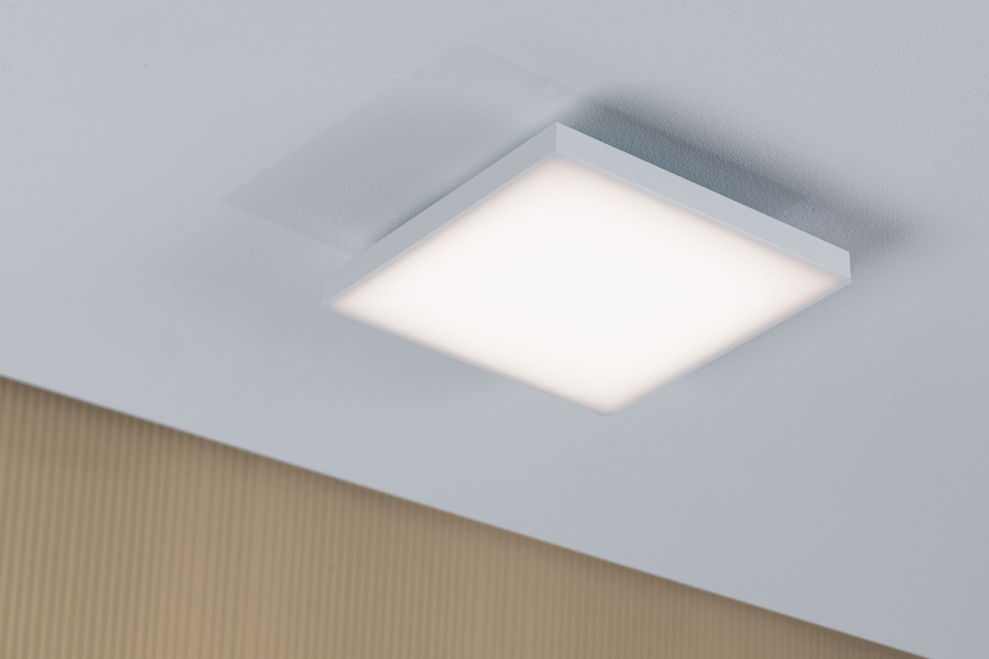 Ein quadratisches Deckenlicht mit weißem Rahmen leuchtet hell auf einer weißen Decke.