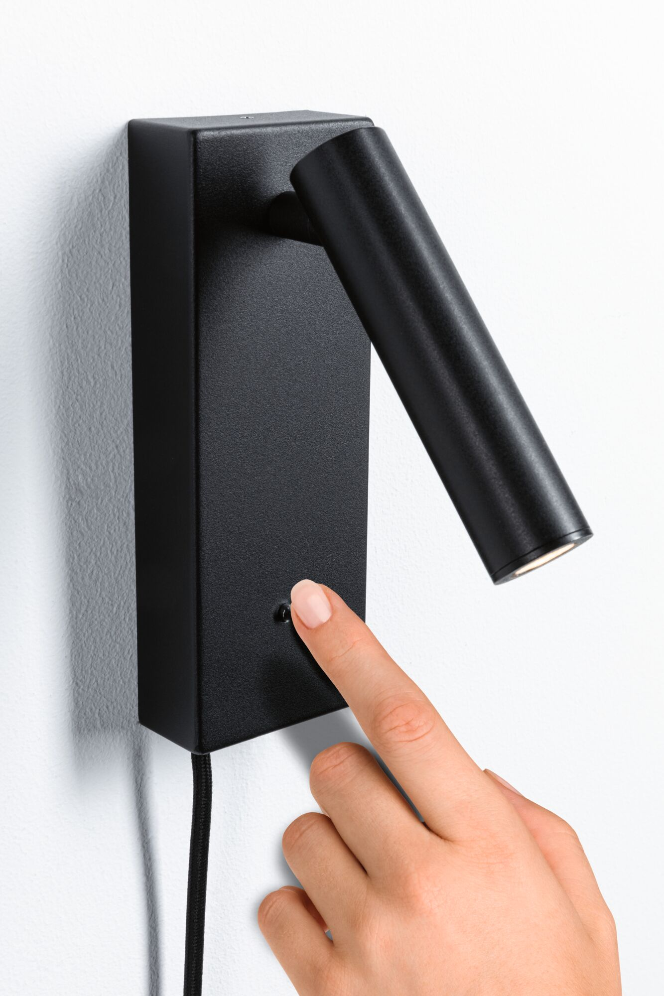 Dłoń naciska przycisk na czarnej lampie ściennej.