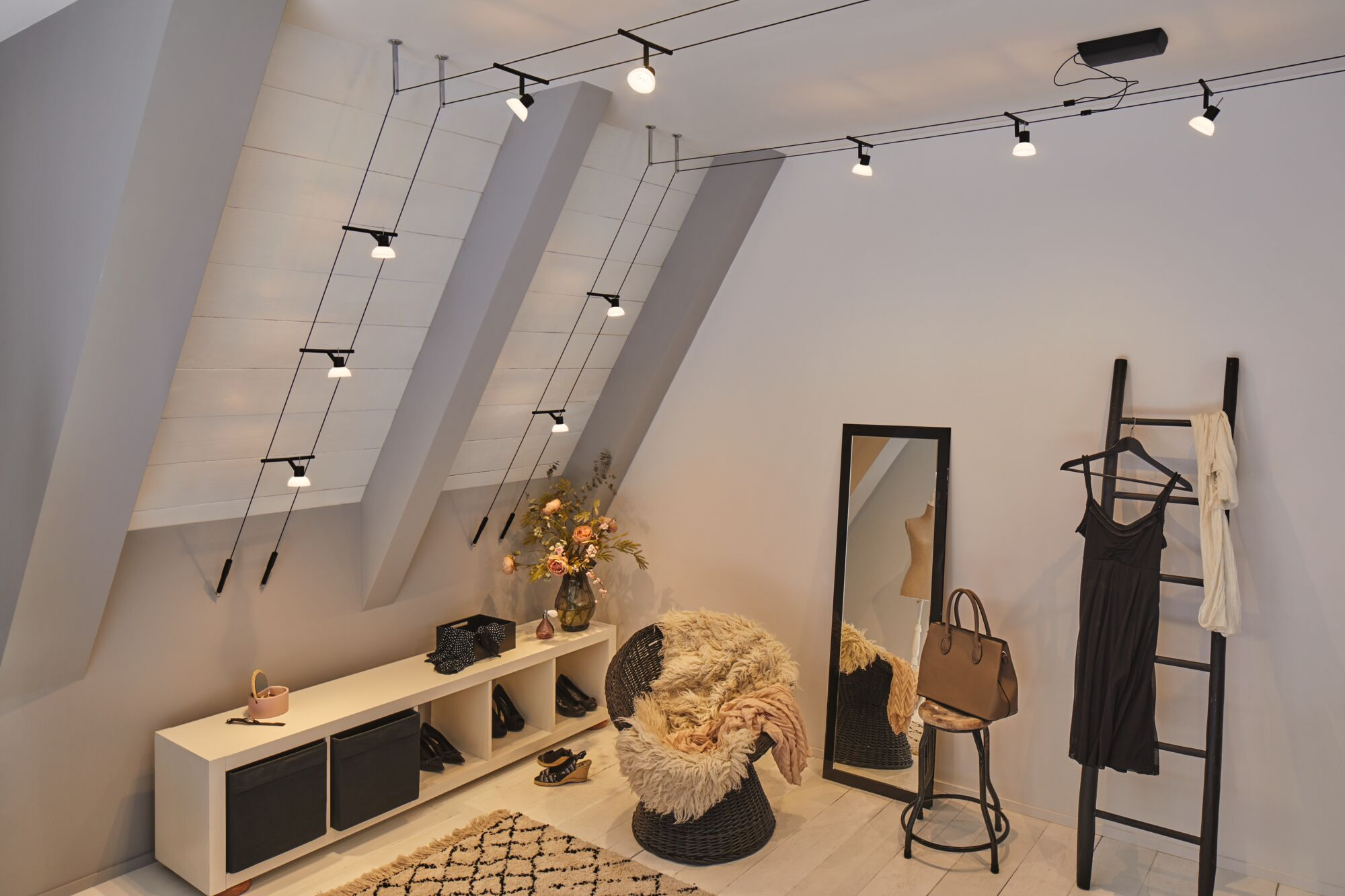 Un camerino mansardato con soffitto spiovente, faretti, sedia, specchio e scala per abiti.