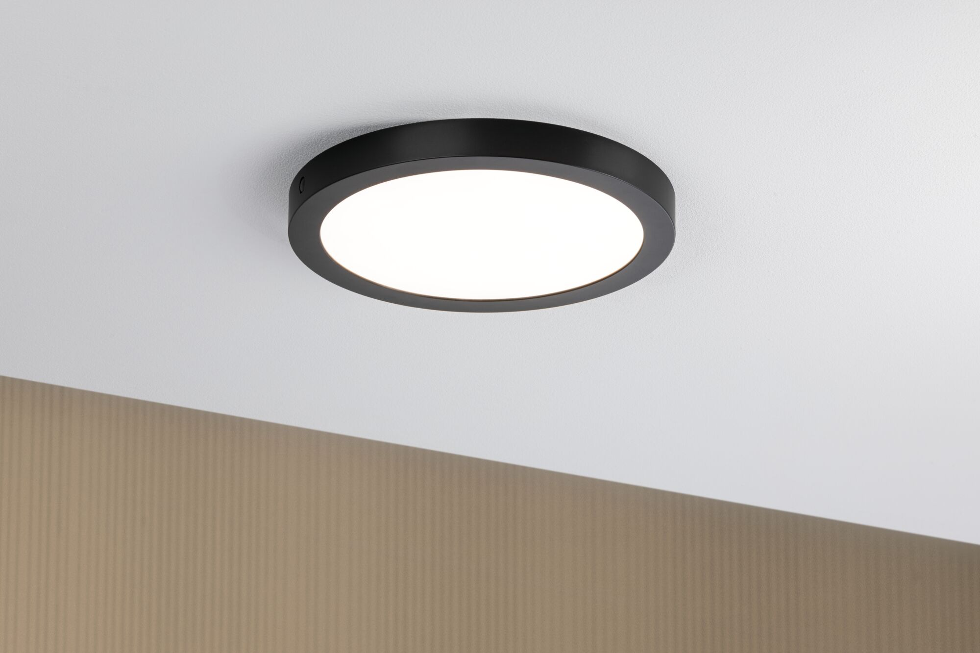 Una lampada da soffitto rotonda e nera con luce brillante è su un soffitto bianco.