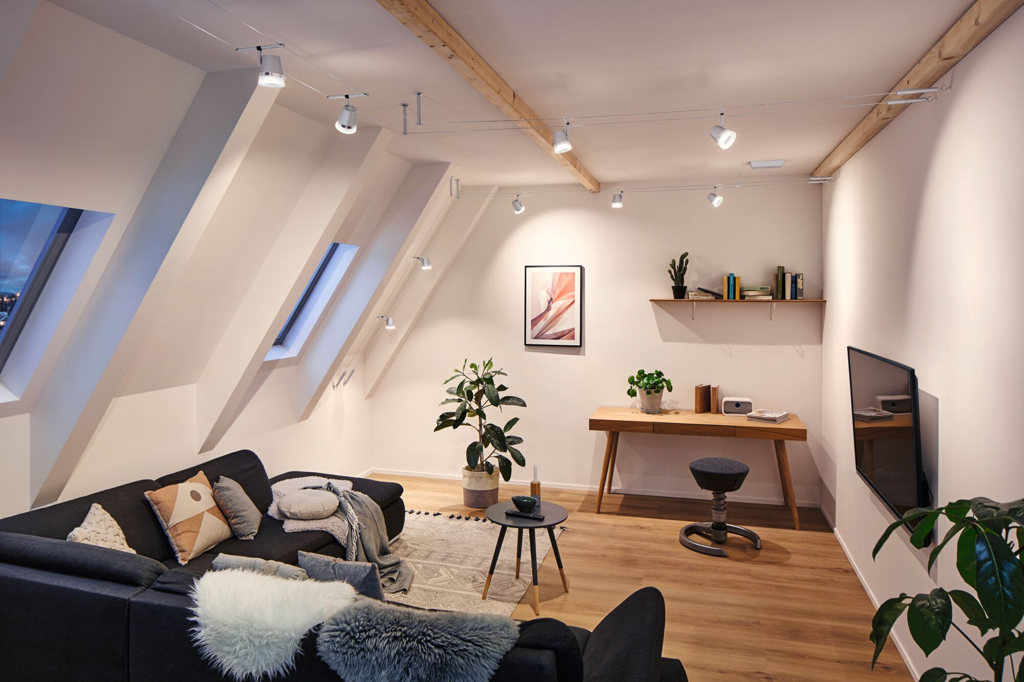 Modernes Wohnzimmer mit Dachschräge, dunklem Sofa, Schreibtisch und Fernseher.