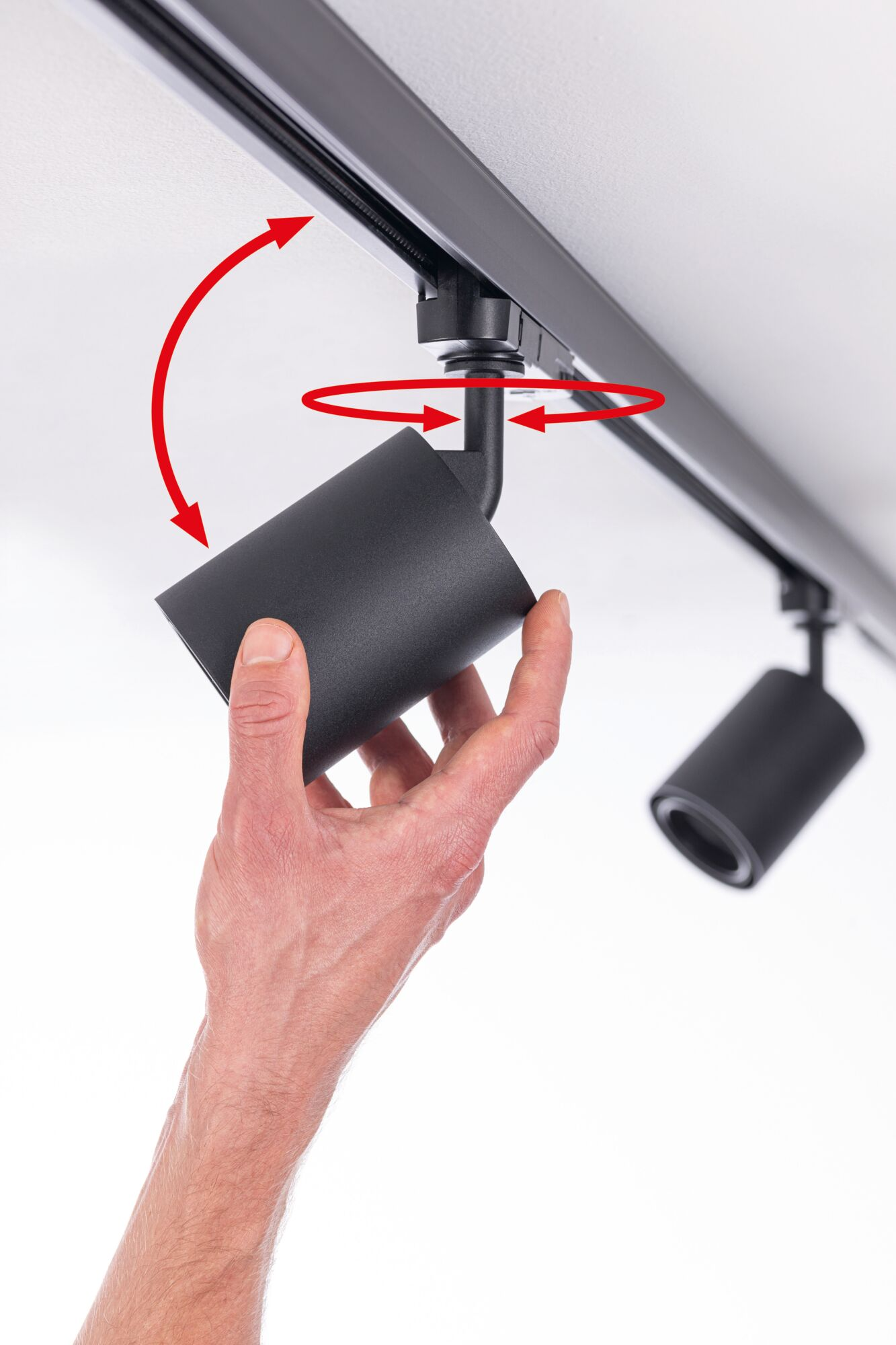 Ręka reguluje czarny reflektor na szynie. Czerwone strzałki wskazują ruch.