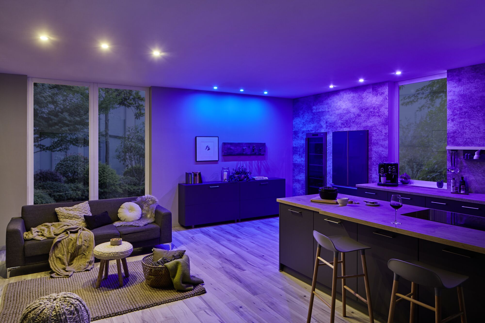 Un soggiorno e una cucina moderni, illuminati da luce blu e viola.