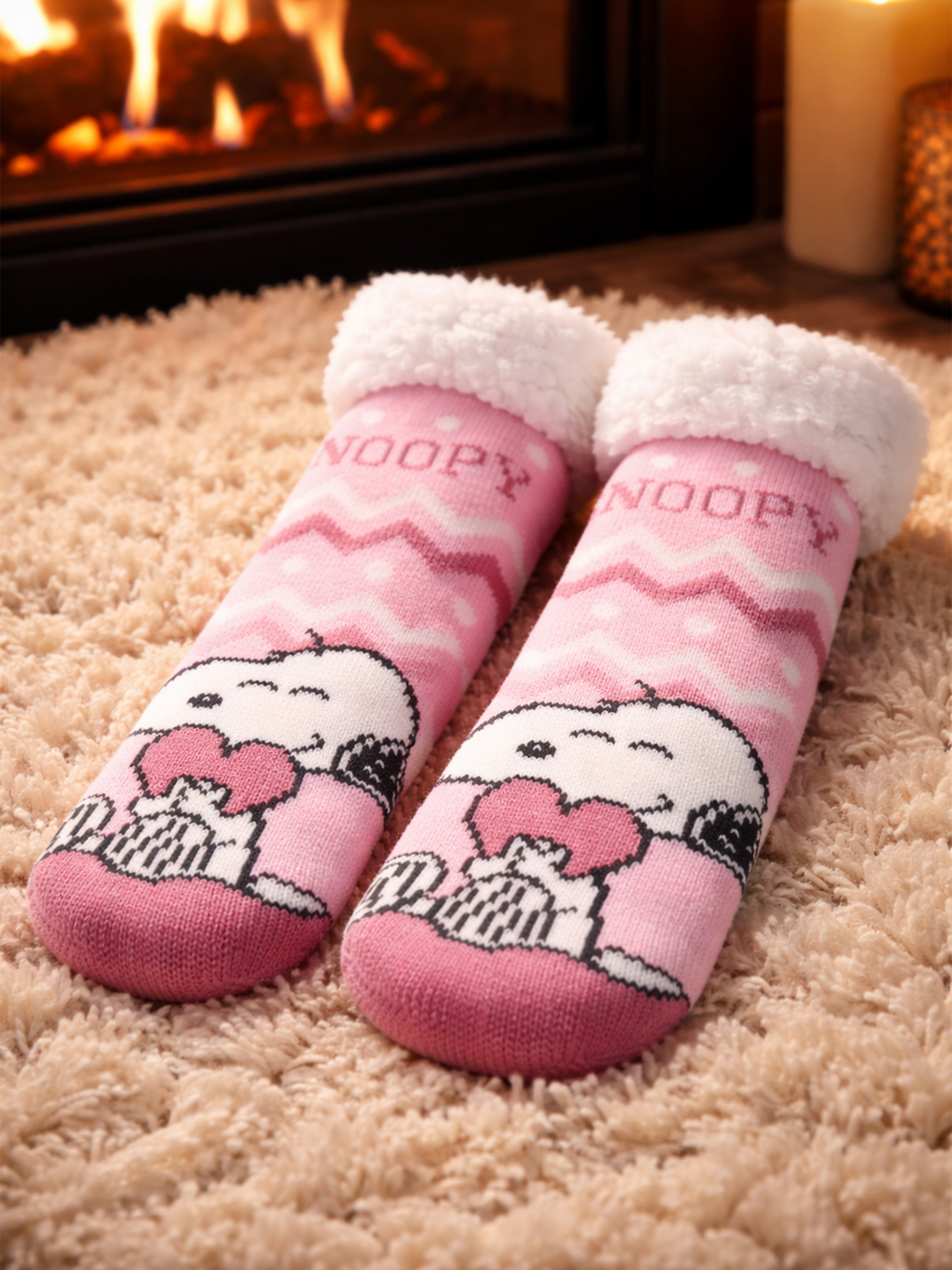 Rosa Snoopy-Socken mit weißen flauschigen Bündchen auf einem beigen Teppich.