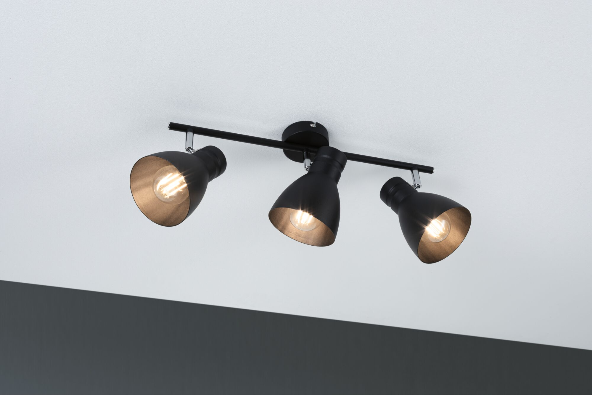 Faretti da soffitto neri con tre teste orientabili e lampadine a vista.