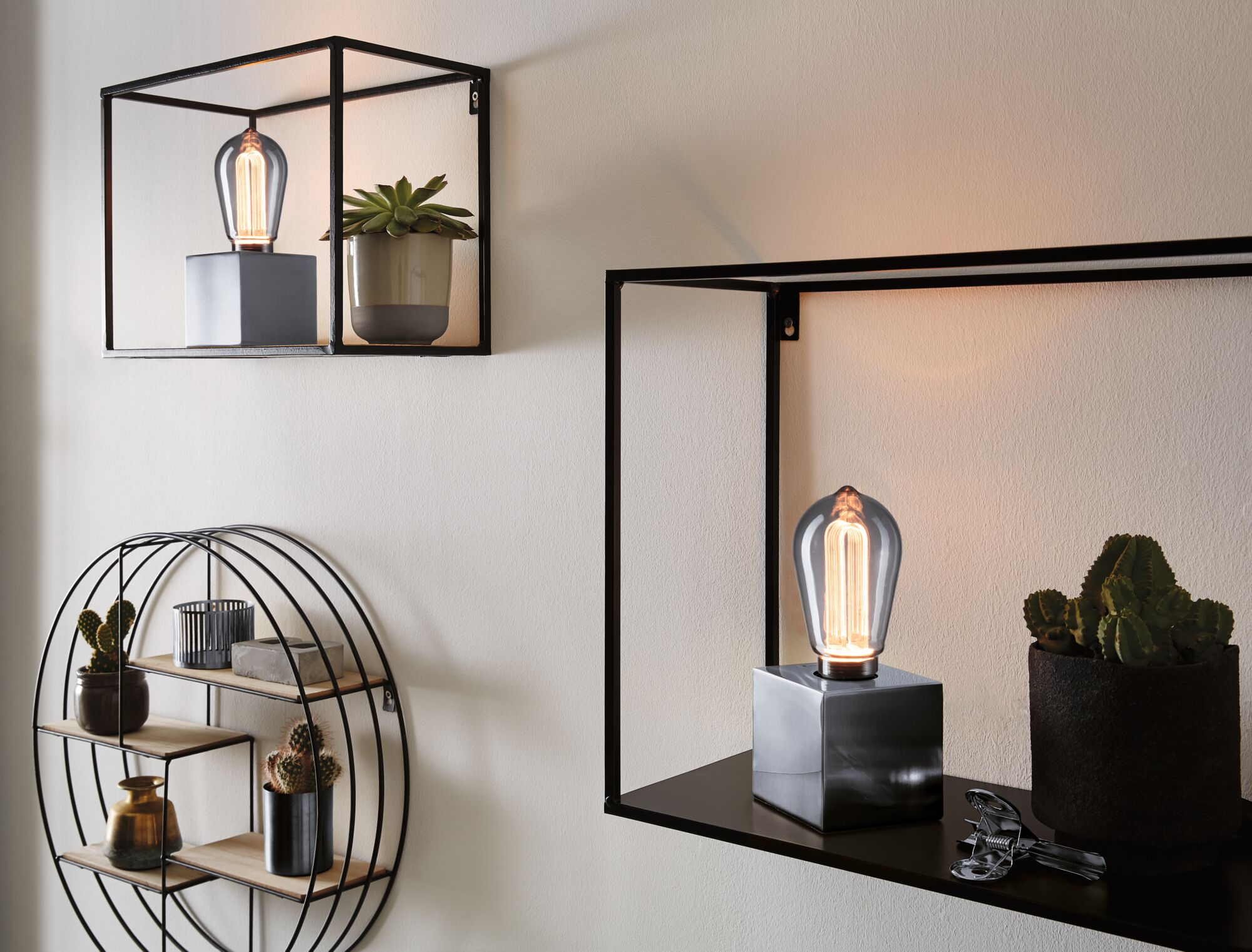 Zwei schwarze Wandregale mit Dekoartikeln, darunter Lampen und Pflanzen.