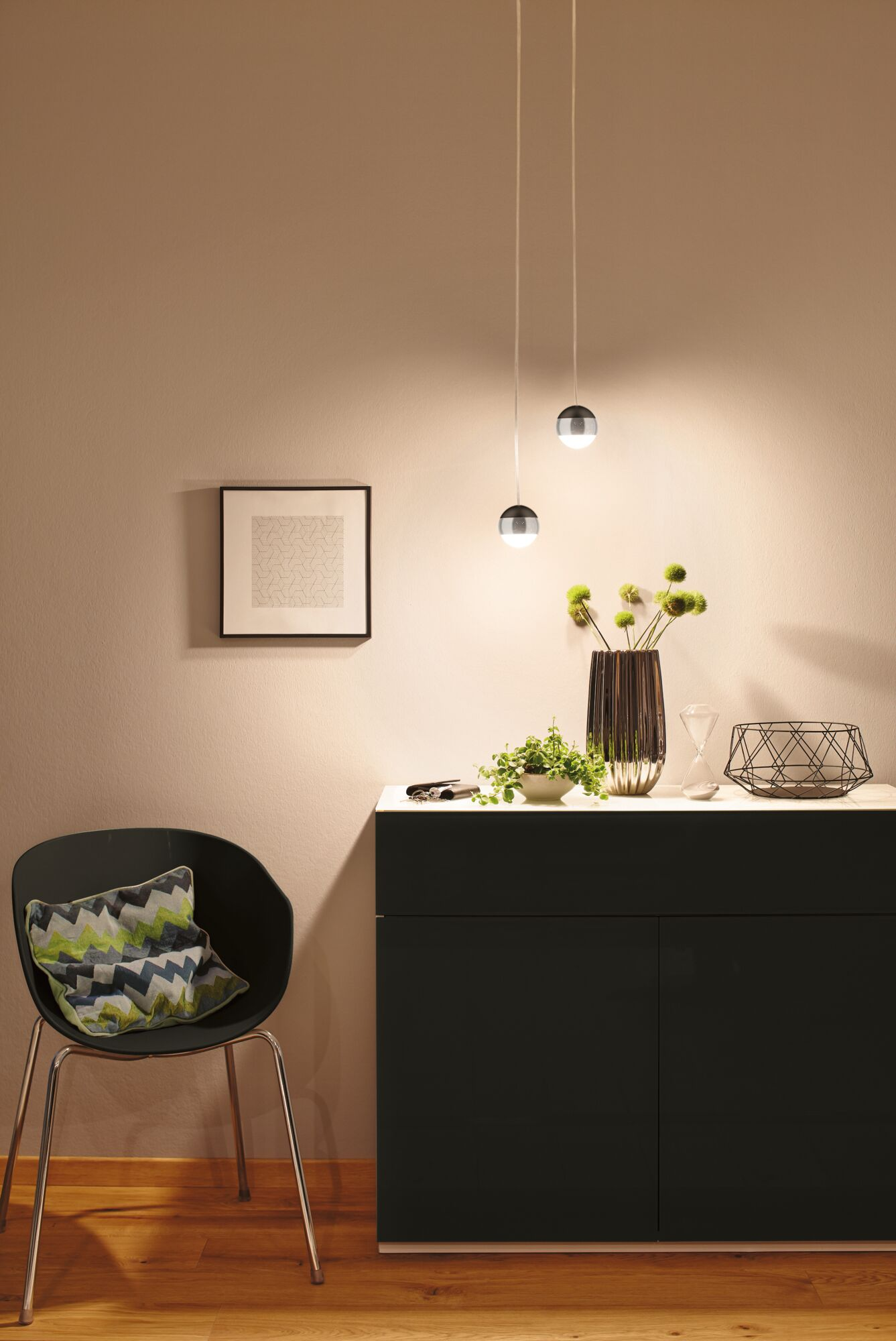 Ein schwarzer Schrank mit Deko, ein Stuhl mit Kissen und Bilder an der Wand.