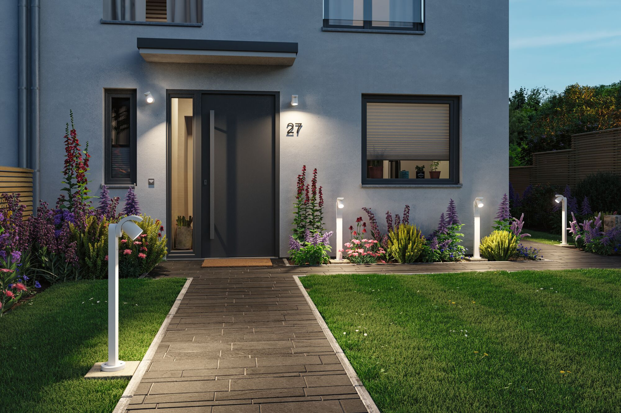 Kamienna ścieżka prowadzi do szarych drzwi wejściowych z numerem 27. Oświetlone lampy wzdłuż ścieżki.