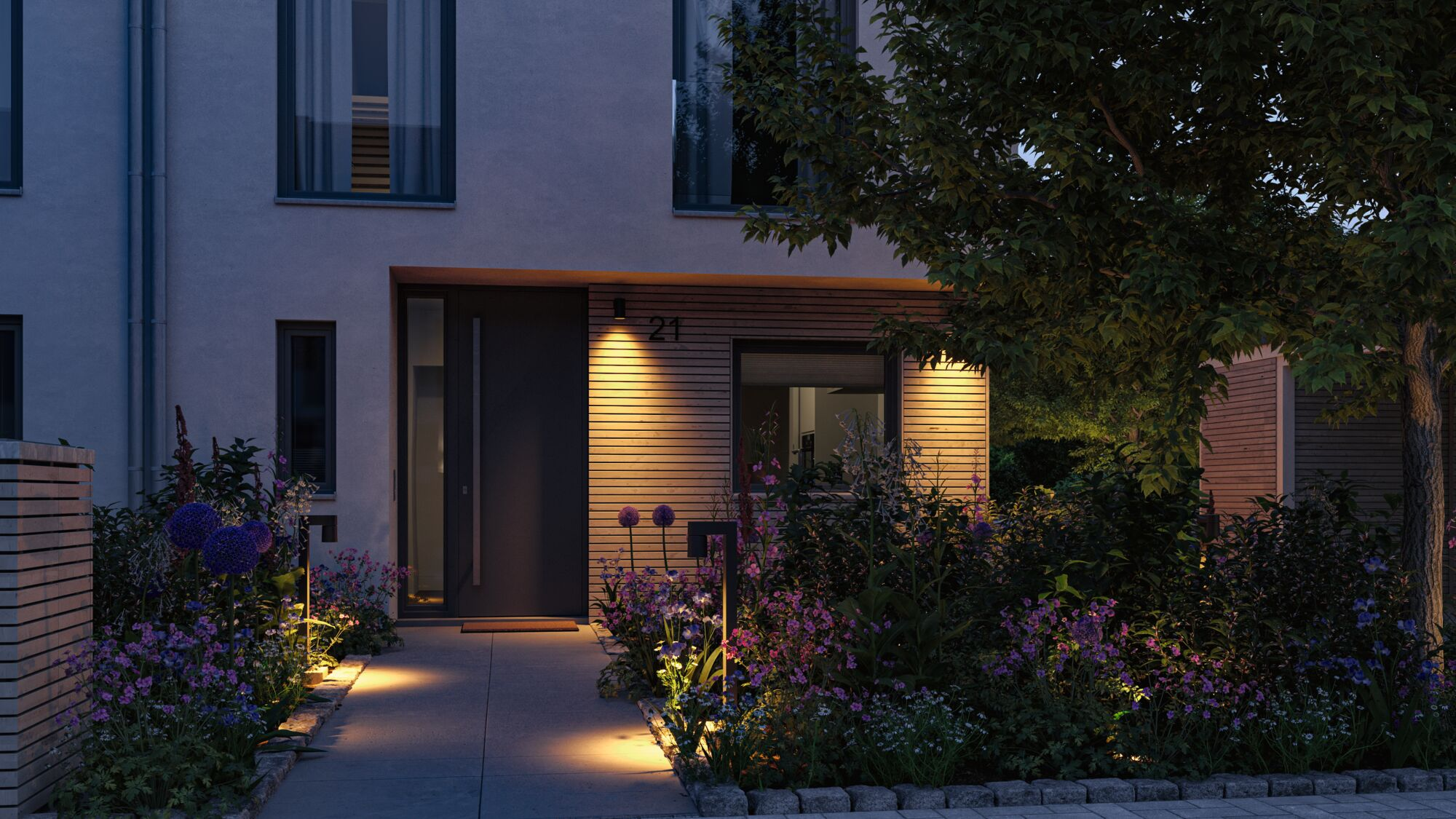 Dom ze światłami, kwiatami i drzewem w nocy.