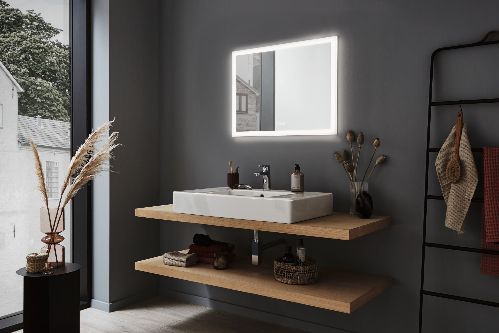 Modernes Badezimmer mit weißem rechteckigem Waschbecken, beleuchtetem Spiegel, Holzregalen und Deko.