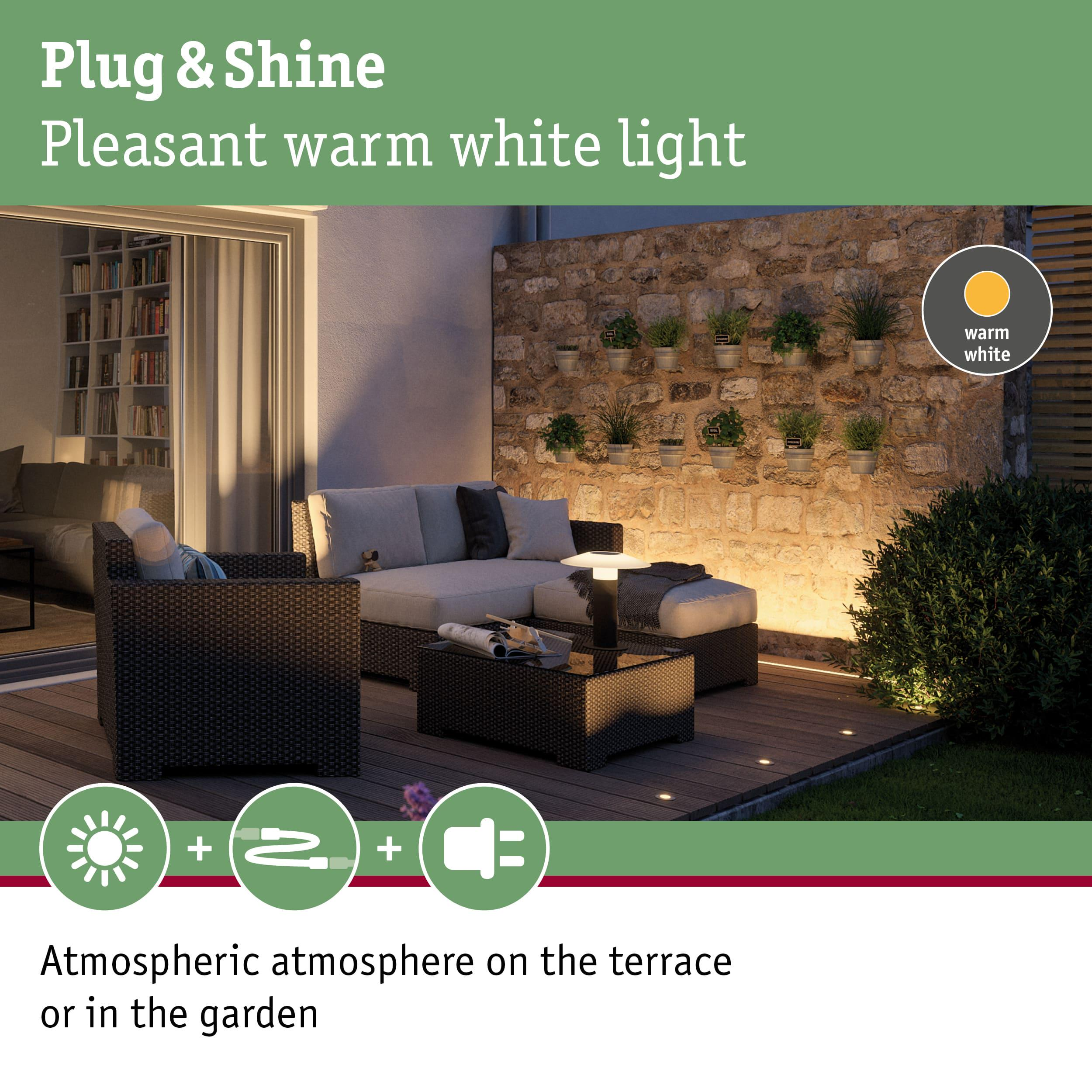 Terrassenmöbel mit warmweißer Beleuchtung vor Steinwand mit Pflanzen.