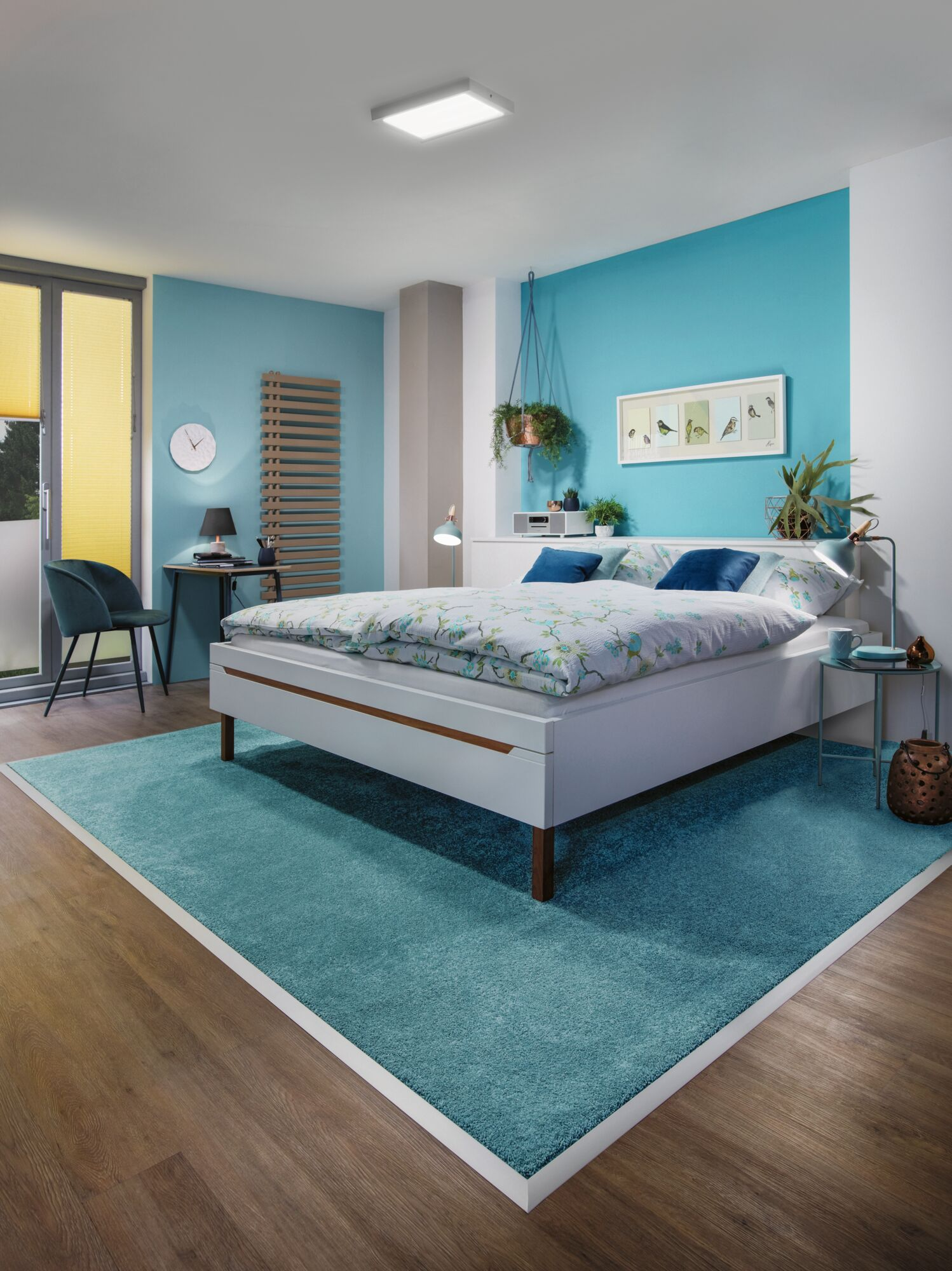 Modernes Schlafzimmer mit blauem Teppich, Bett, Schreibtisch und Fenster.
