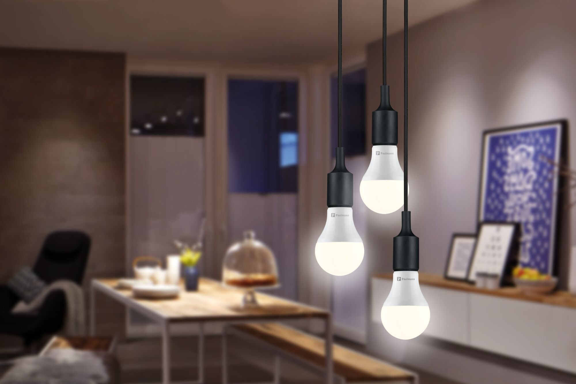 Drei Paulmann LED-Lampen hängen an schwarzen Kabeln über einem Esstisch.