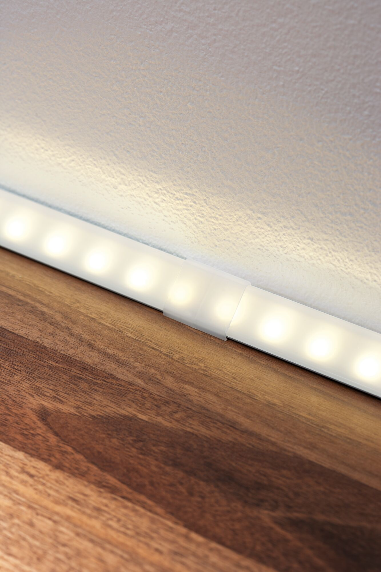 Pasek LED świeci na drewnie przy białej ścianie.