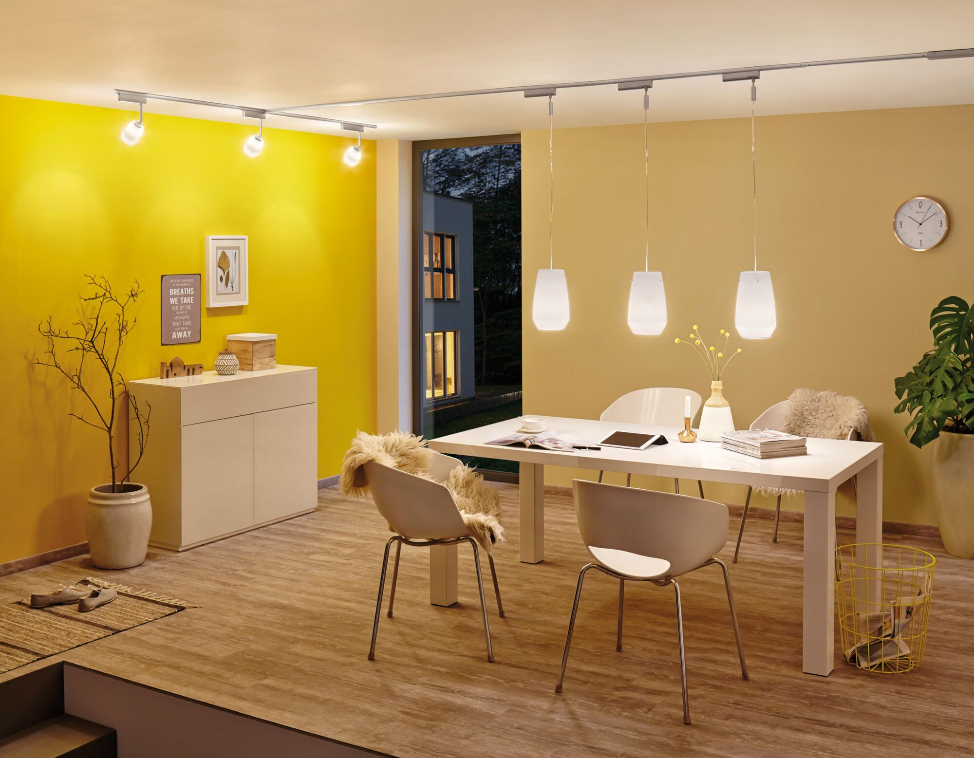 Jadalnia z żółtymi ścianami, białym stołem i krzesłami, lampami wiszącymi.