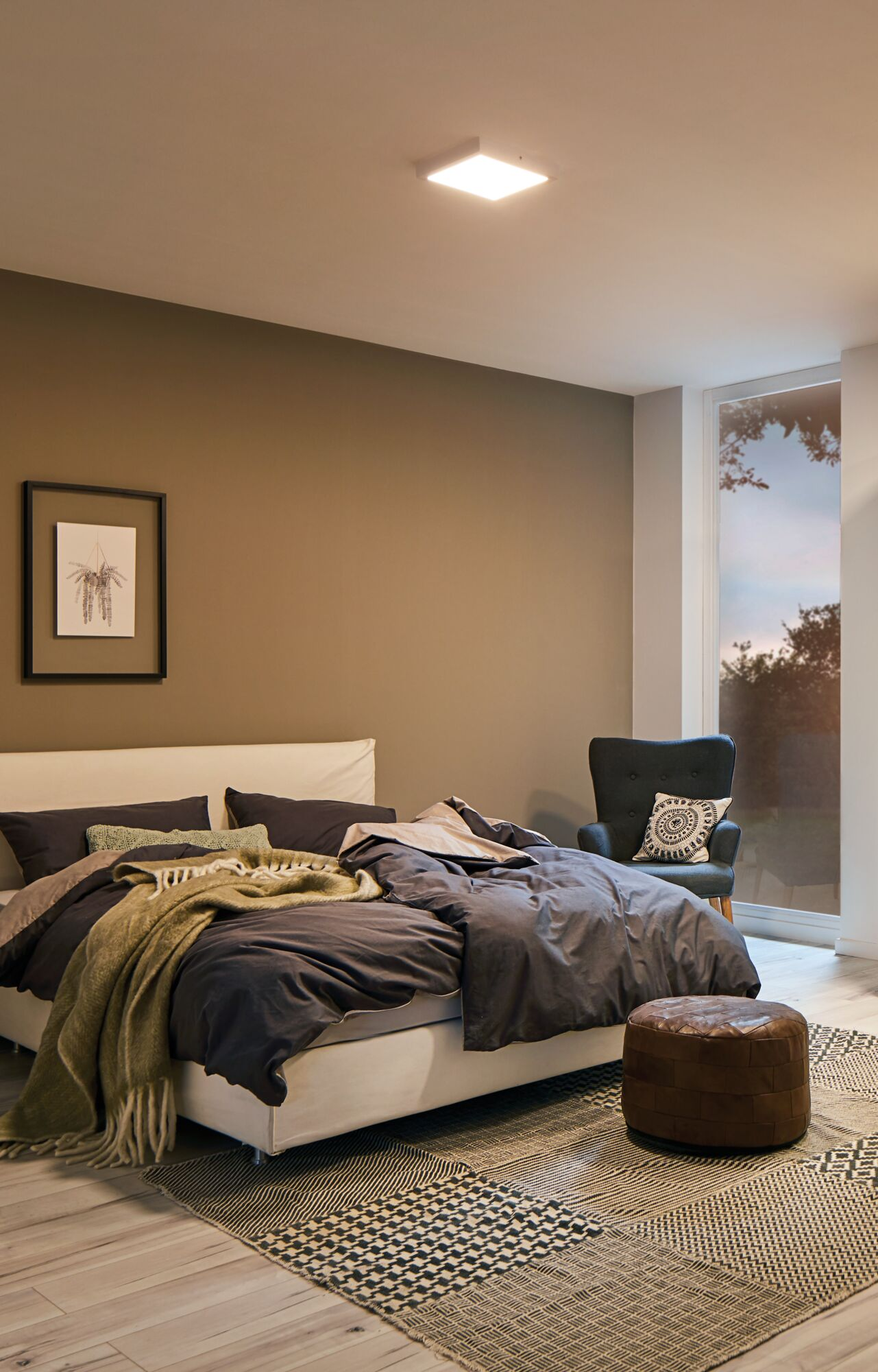 Ein Schlafzimmer mit einem Bett, Sessel, Hocker und einem großen Fenster.
