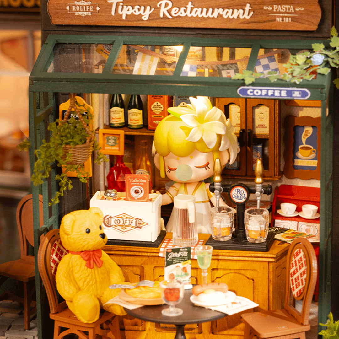 Ein Bären-Plüschtier sitzt an einem Tisch in einem Miniatur-Restaurant mit einer Puppe hinter der Theke.