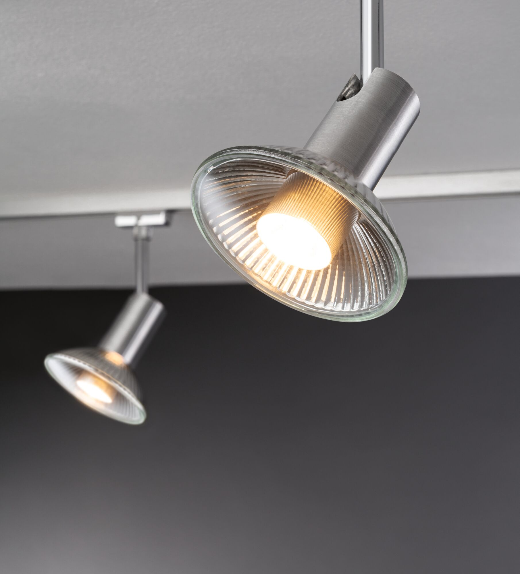 Dwa srebrne reflektory sufitowe ze szklanymi odbłyśnikami i zapalonymi żarówkami.