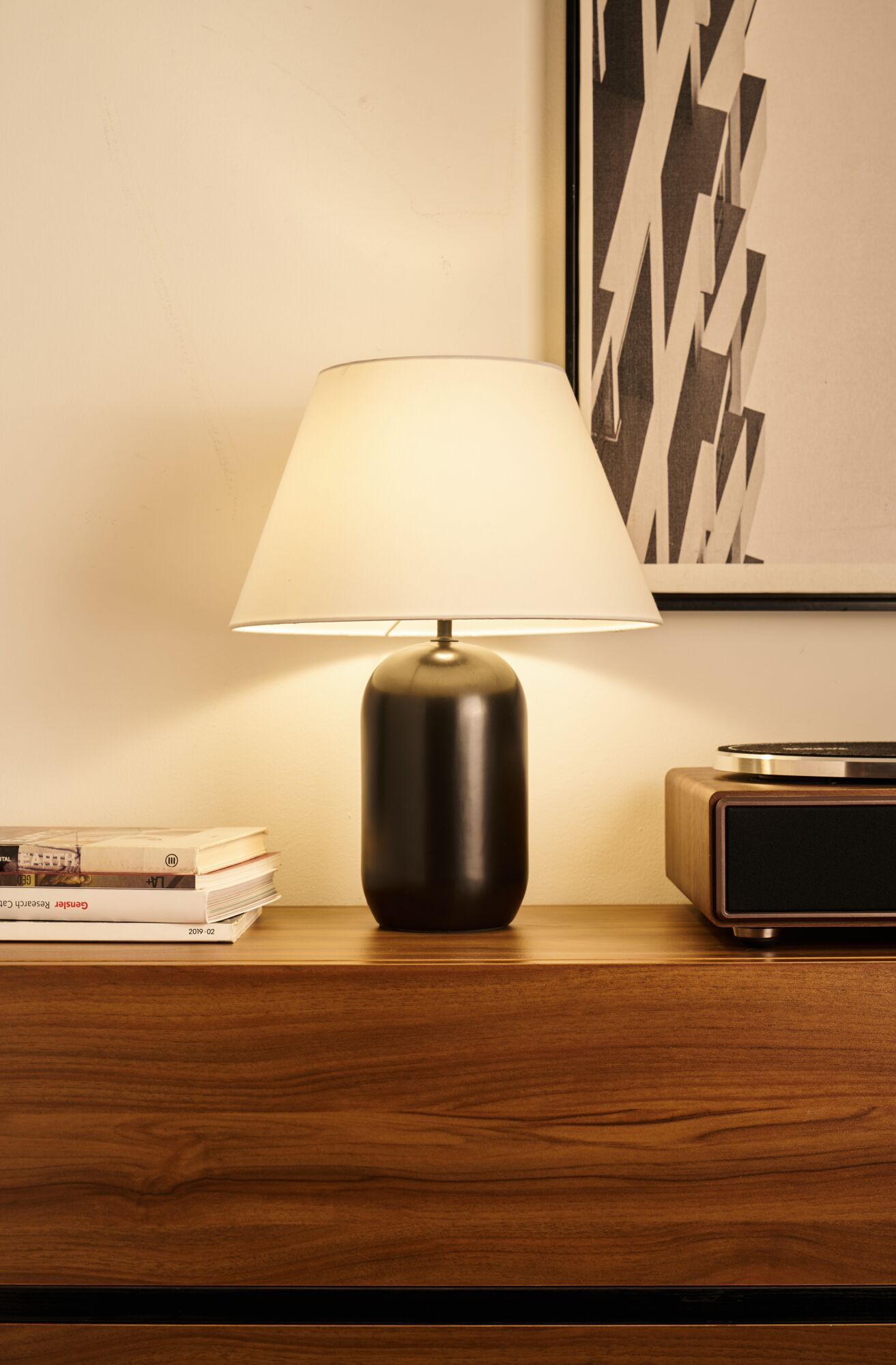 Ciemny stolik nocny z lampą, książkami i gramofonem.