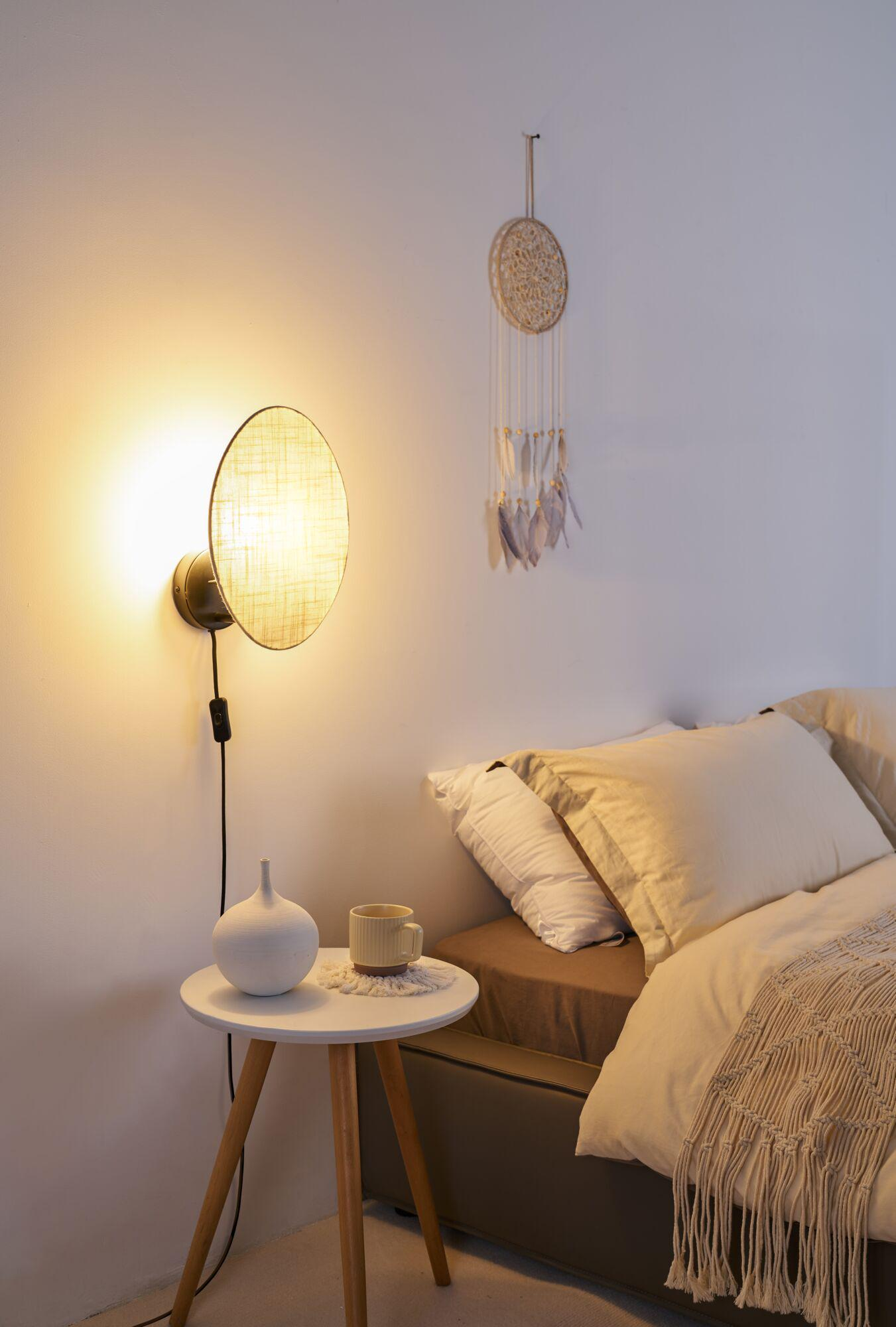 Stolik nocny z wazonem i filiżanką obok łóżka z poduszkami i kocem.