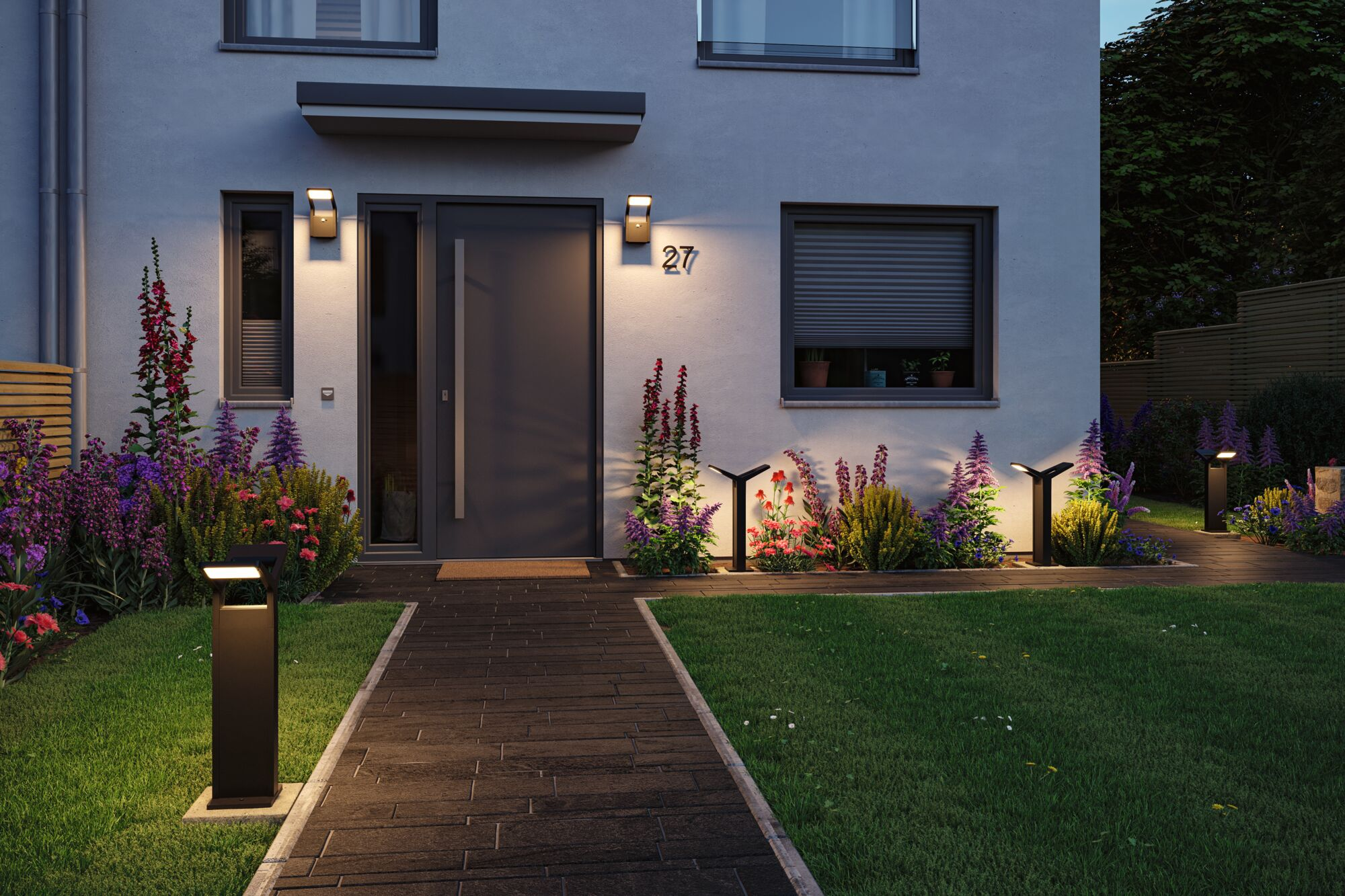 Nowoczesny dom z oświetlonym wejściem, kwiatami i lampami przy ścieżce o zmierzchu.