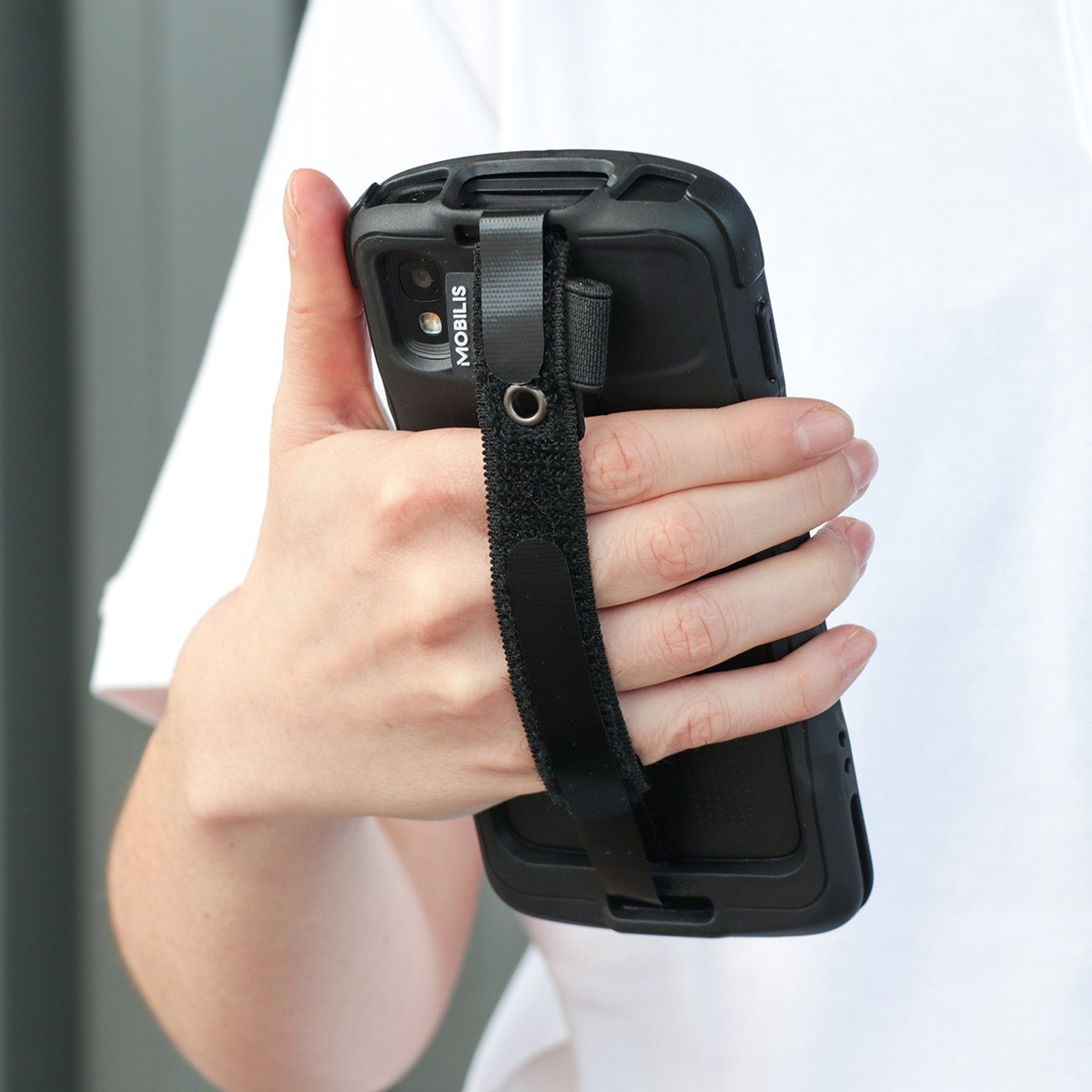 Eine Hand hält ein schwarzes Handy mit einem Riemen. Der Riemen ist mit Klettverschluss befestigt.