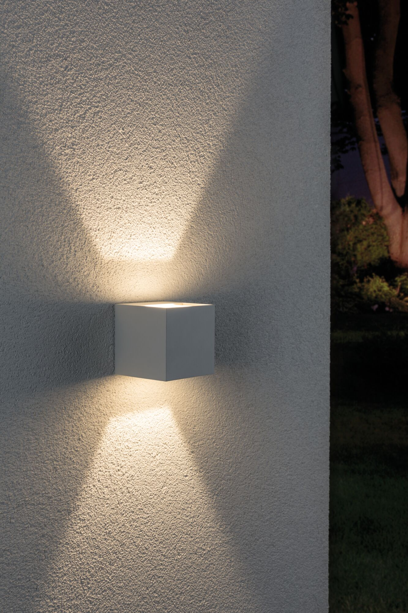 Una lampada da parete esterna cubica proietta luce verso l'alto e verso il basso su una parete ruvida.
