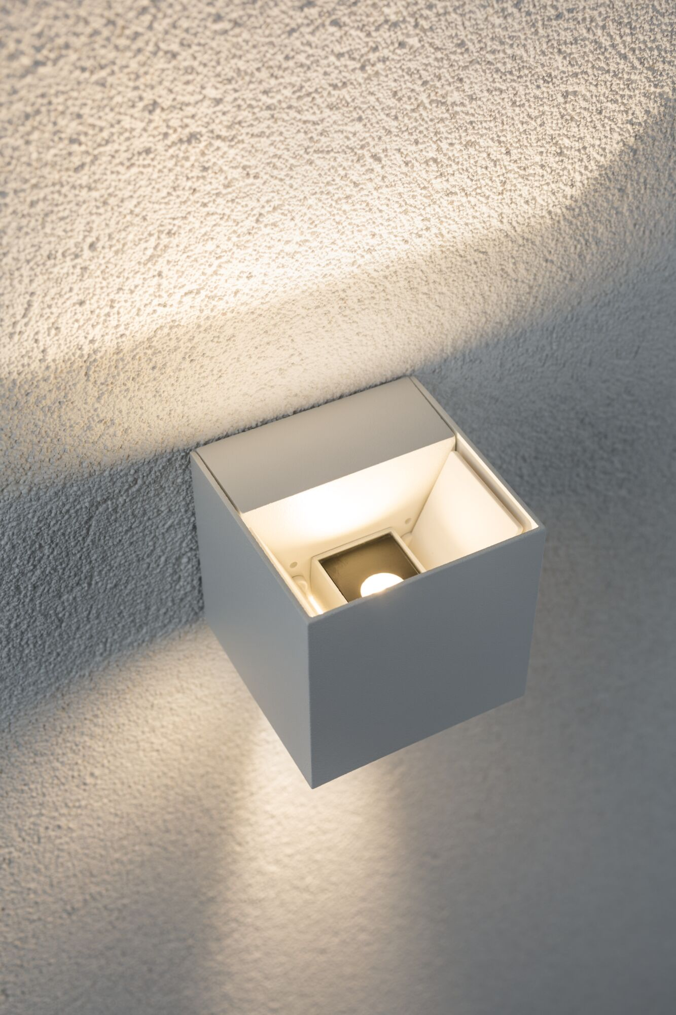 Una lampada da parete bianca a cubo illumina una parete testurizzata.
