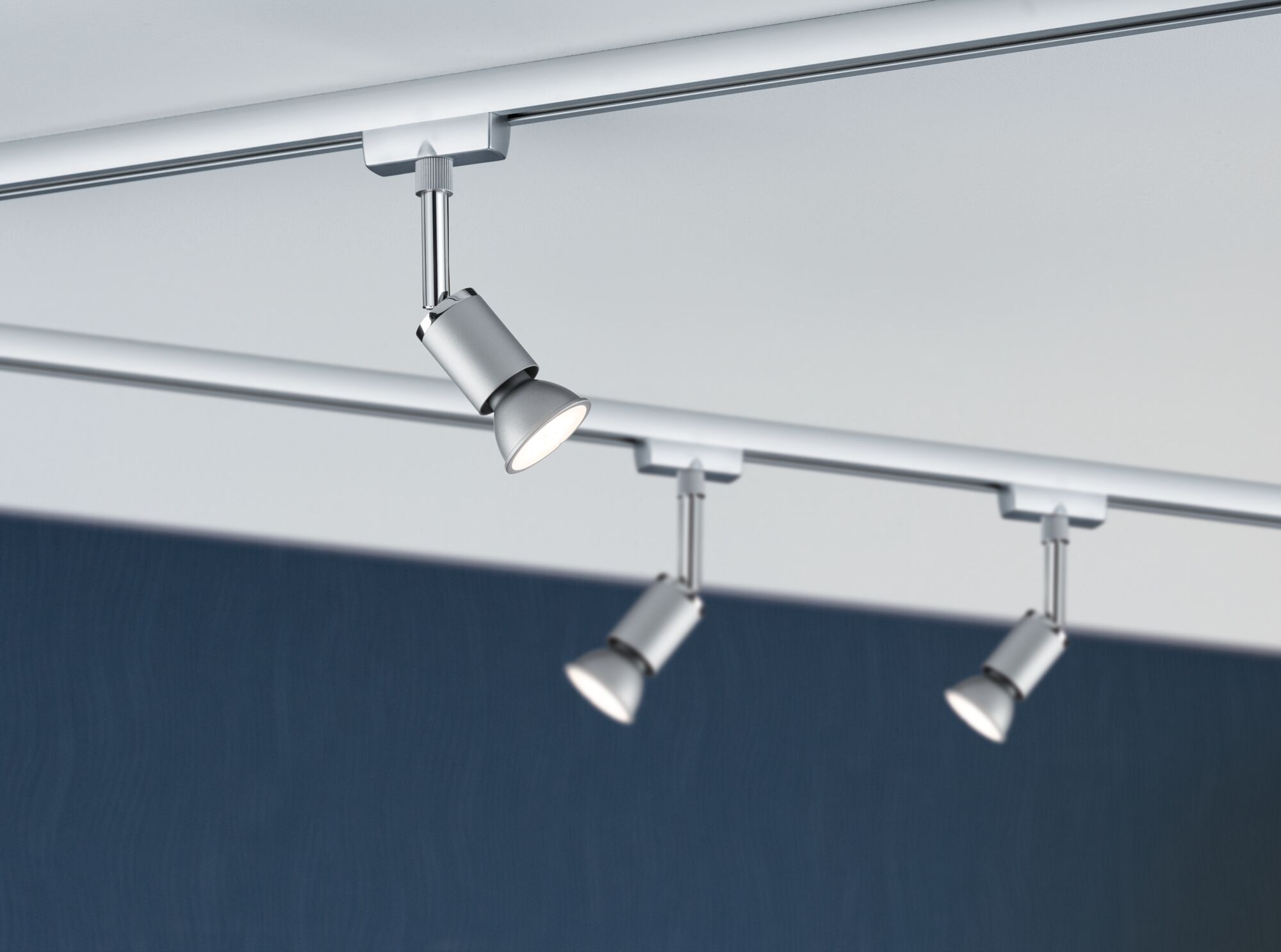 Tre faretti argentati illuminano da un soffitto.