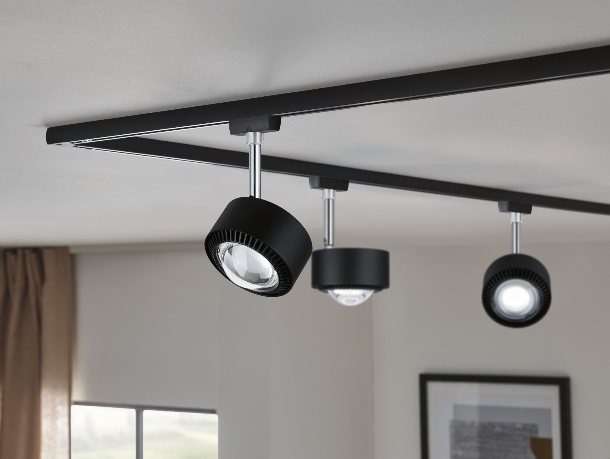 Drei schwarze Schienenstrahler sind an einer schwarzen Schiene an der Decke montiert.