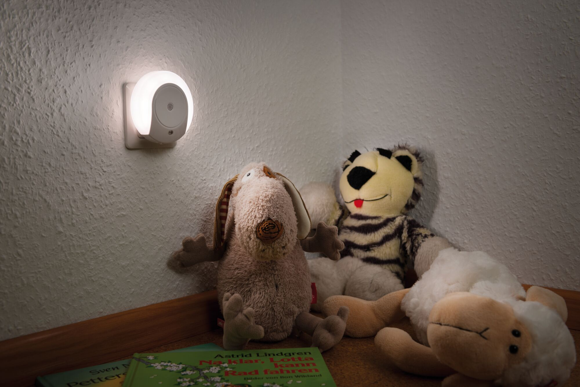 Ein Nachtlicht leuchtet neben Stofftieren und Büchern.