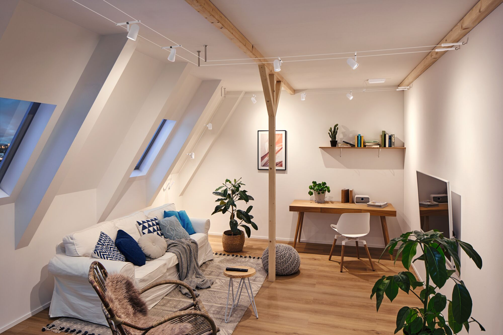 Ein gemütliches Wohnzimmer mit Dachschrägen, Sofa, Schreibtisch und Pflanzen.