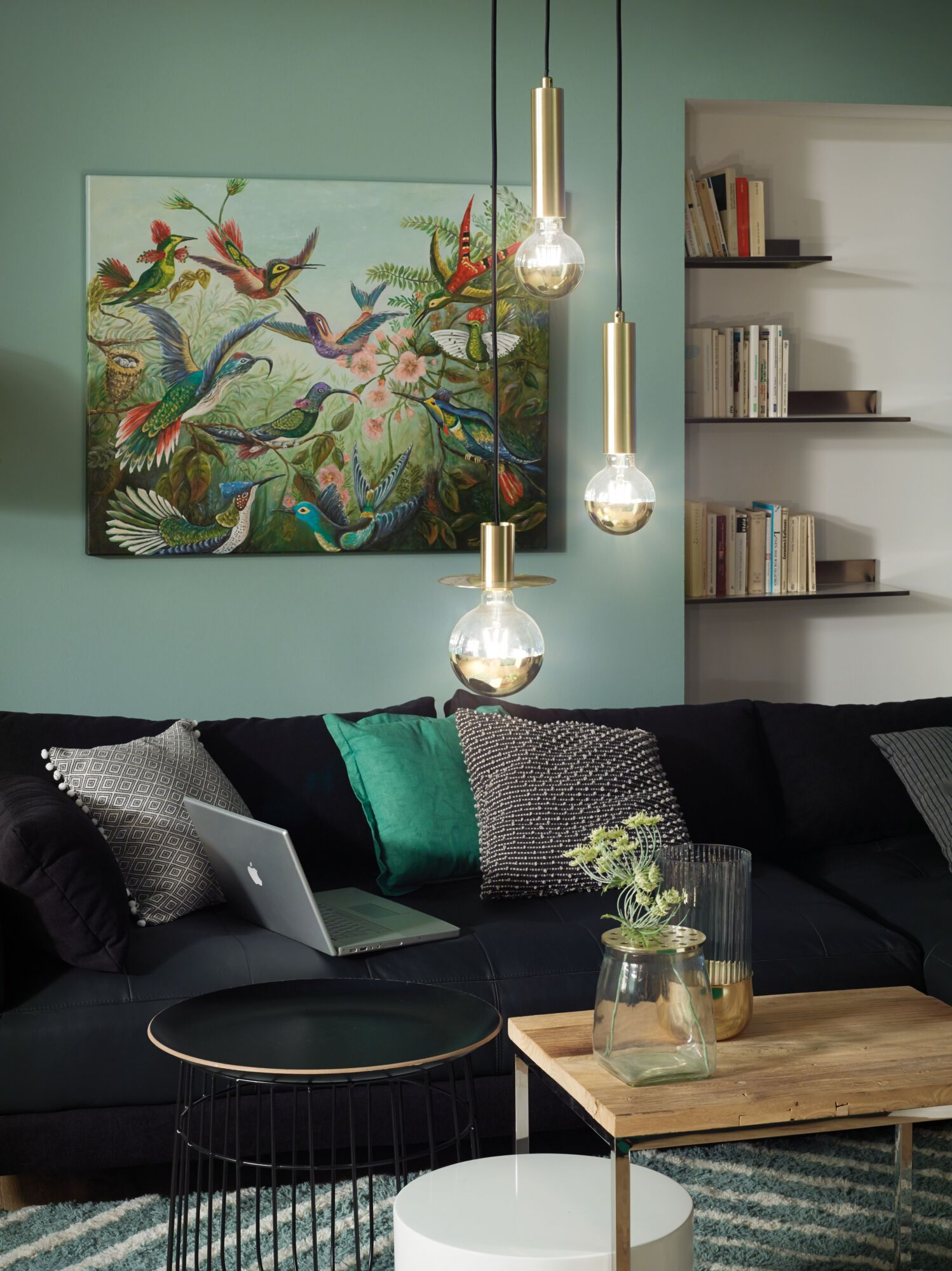 Soggiorno con divano nero, opera d'arte di colibrì, lampade a sospensione e librerie.
