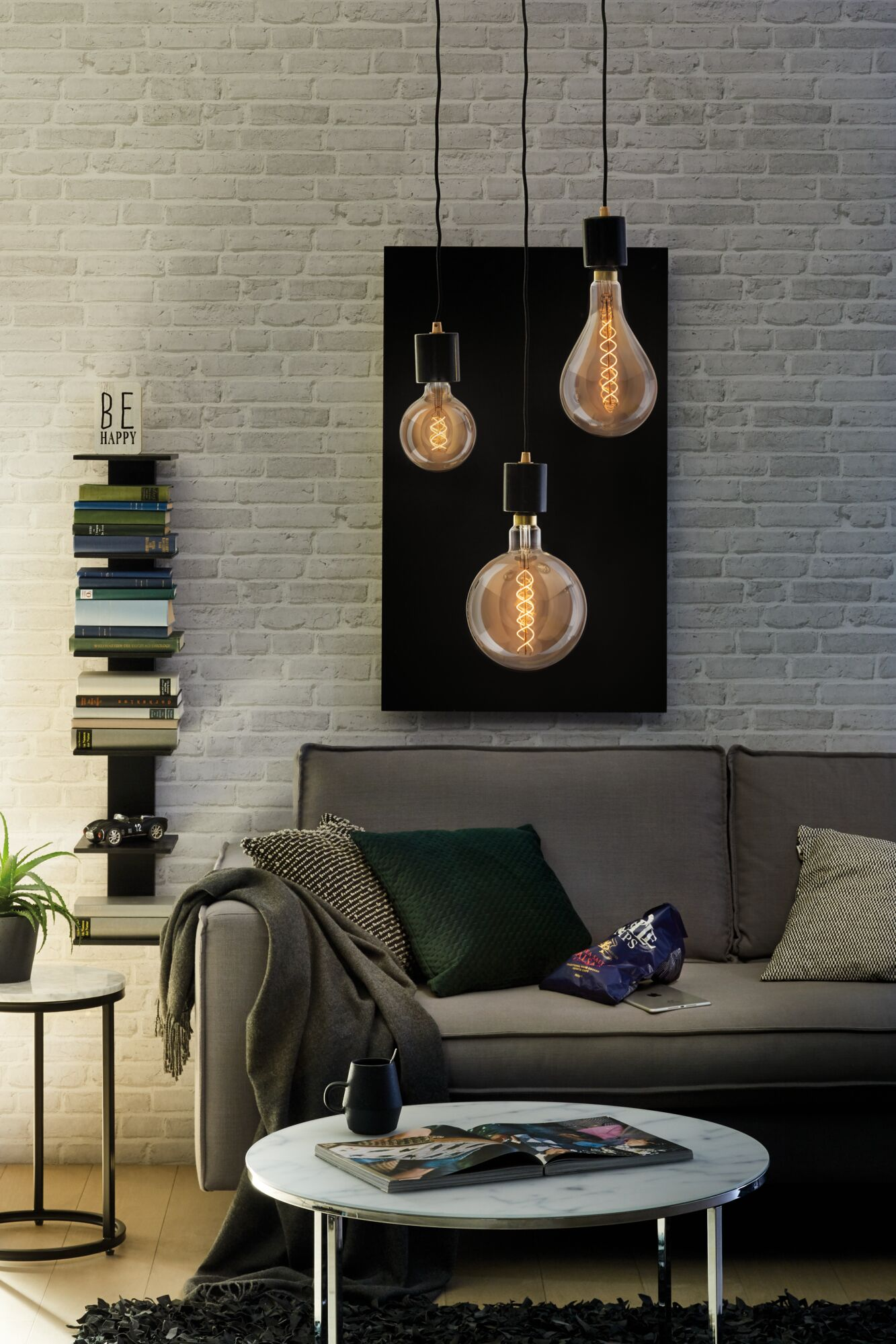 Ein Wohnzimmer mit Ledersofa, Couchtisch, Bücherregal und drei Hängeglühbirnen.