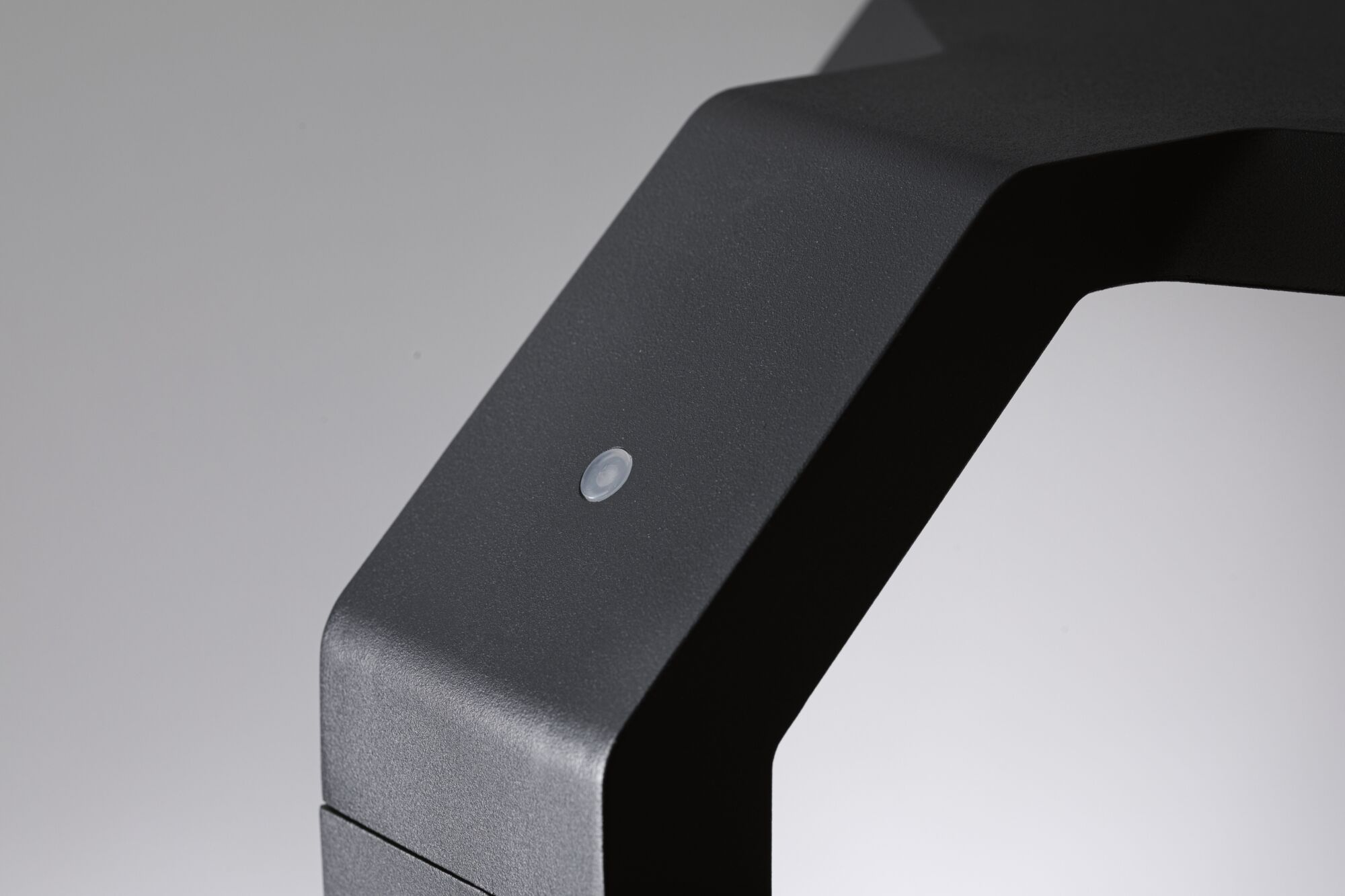 Czarny obiekt z małym białym przyciskiem na szarej powierzchni.