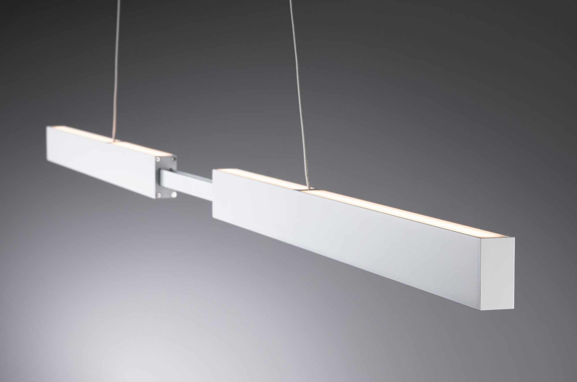 Biała, prostokątna lampa wisząca z dwoma segmentami wisi na cienkich linkach.