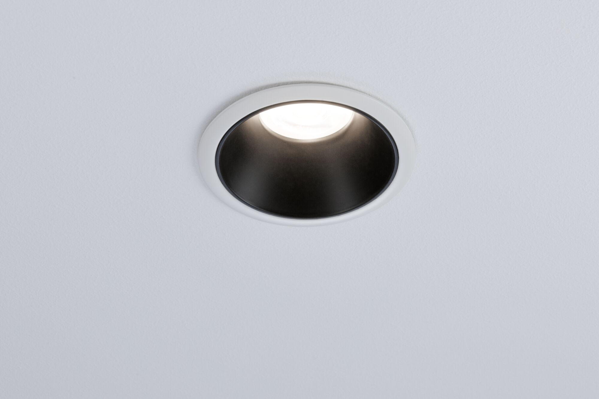Un faretto da incasso con cornice bianca e interno nero illumina un soffitto bianco.