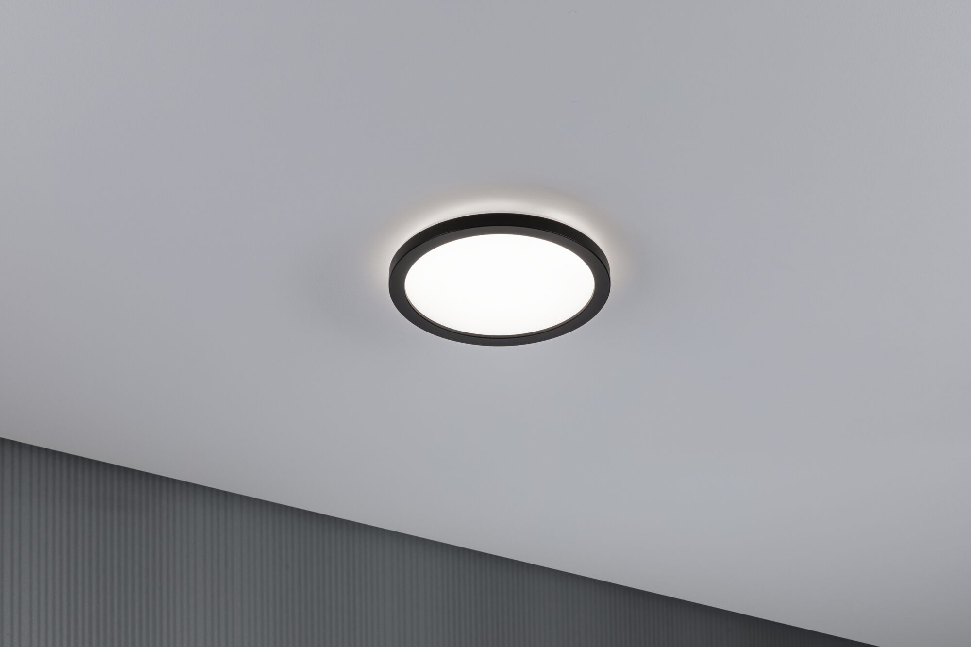 Una lampada da soffitto rotonda con bordo nero brilla su un soffitto bianco.