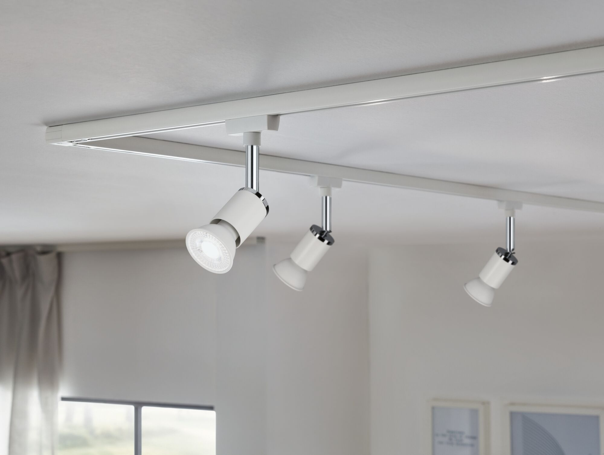 Białe oświetlenie szynowe z trzema regulowanymi reflektorami na suficie.