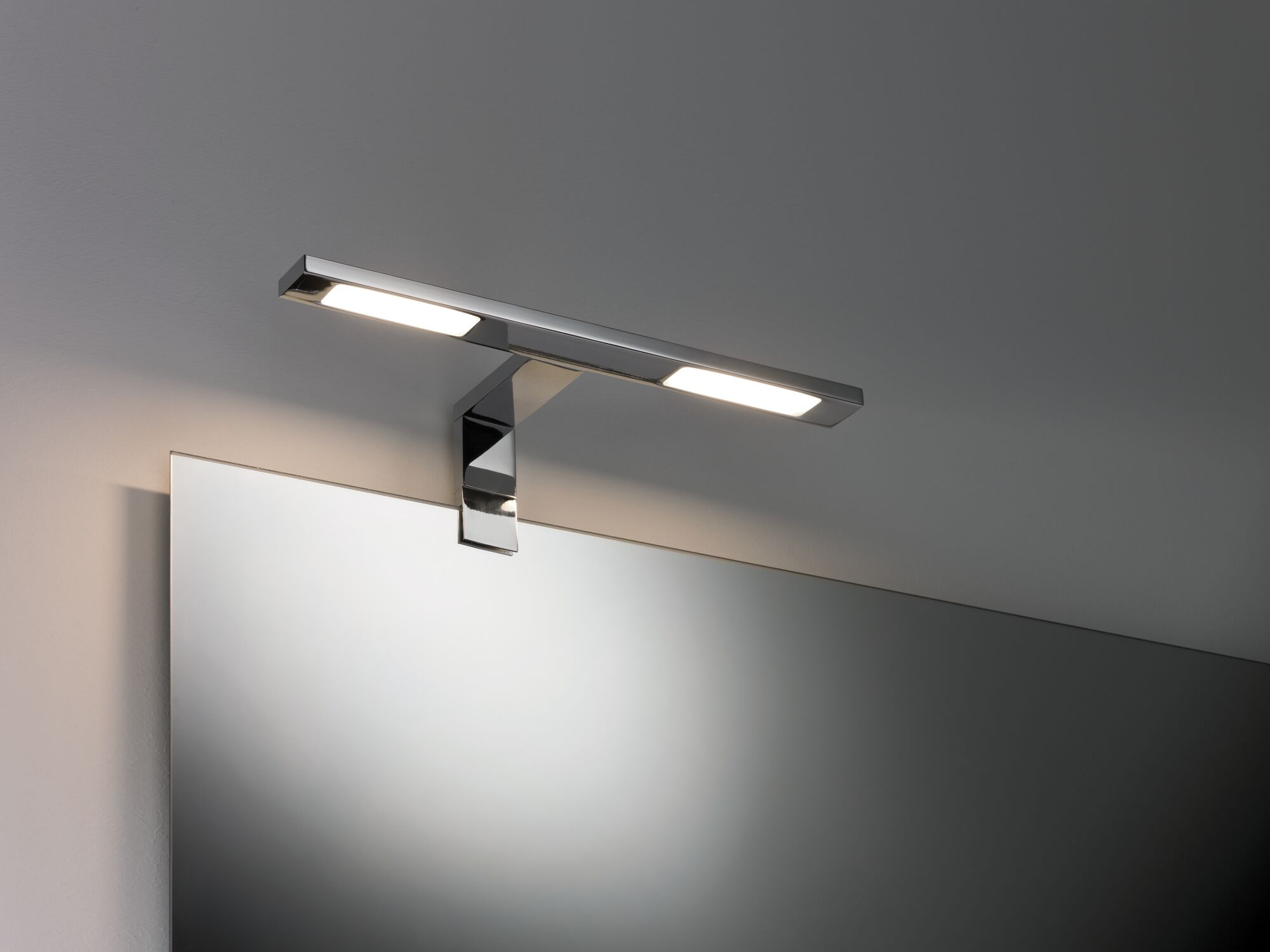 Ein moderner Spiegel mit einer darüber montierten, glänzenden Chrom-Wandleuchte.