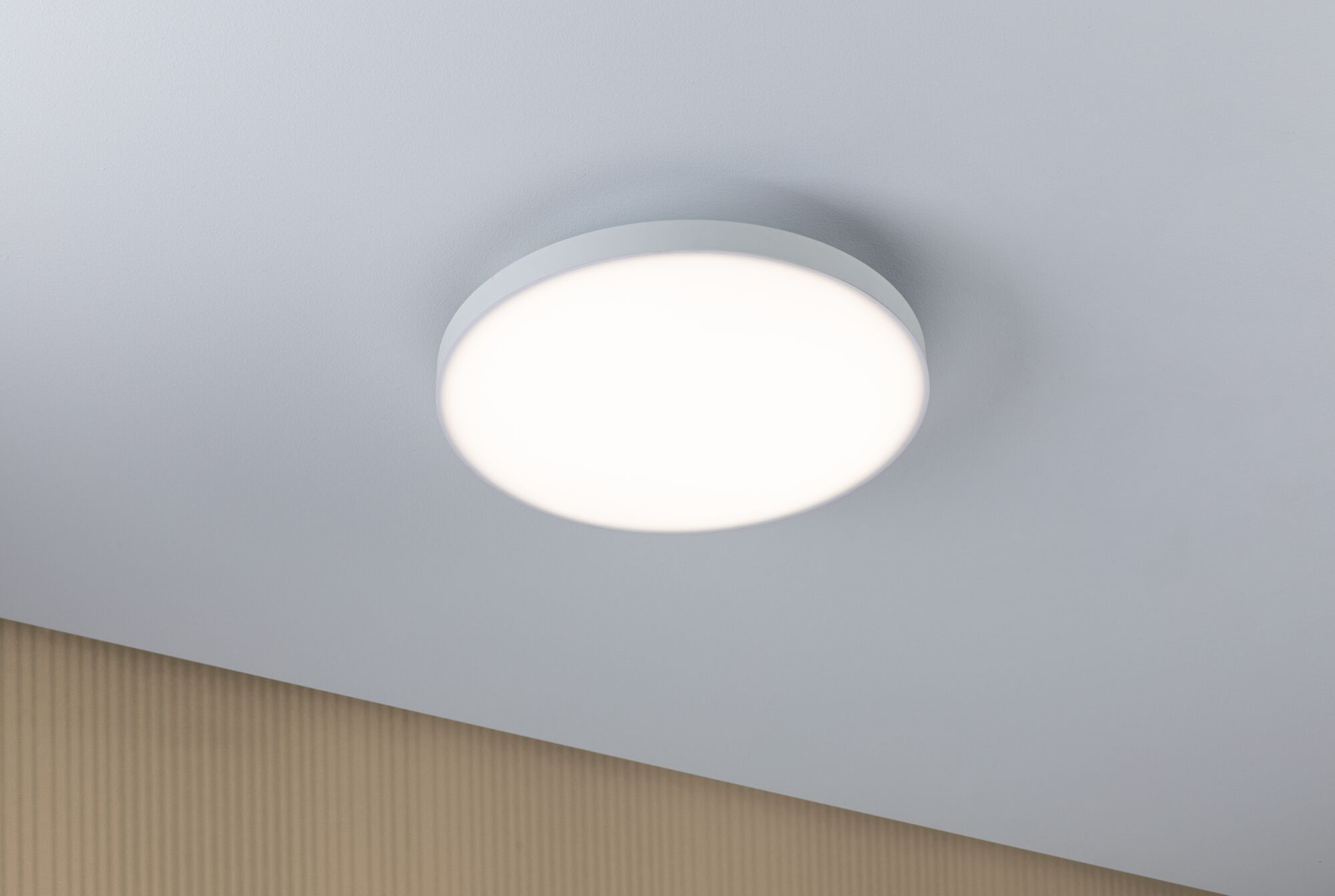 Eine runde, weiße Deckenleuchte mit hellem Licht auf einer weißen Decke.