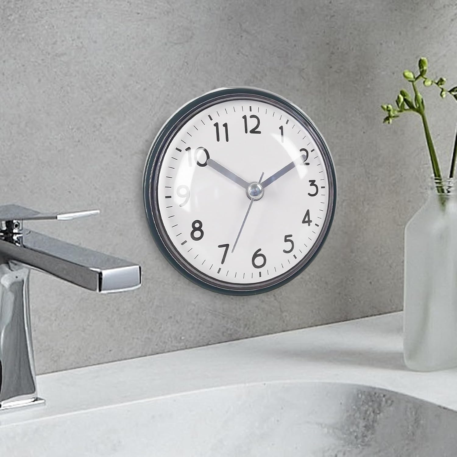 Ein runder Wanduhr mit schwarzen Ziffern hängt an einer grauen Wand.