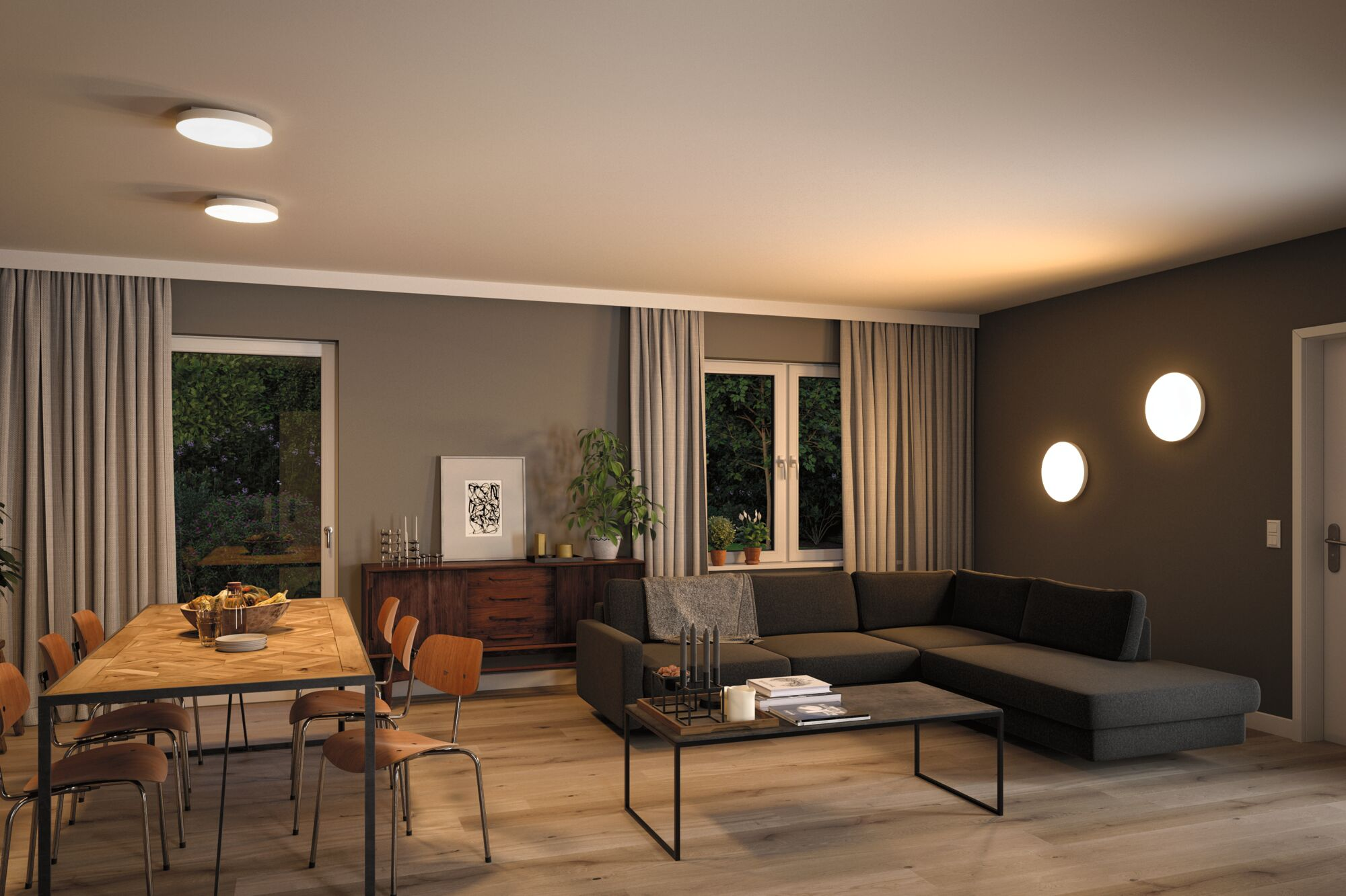 Modernes Wohnzimmer mit Essbereich, dunklem Sofa und Holztisch. Draußen ist es dunkel.