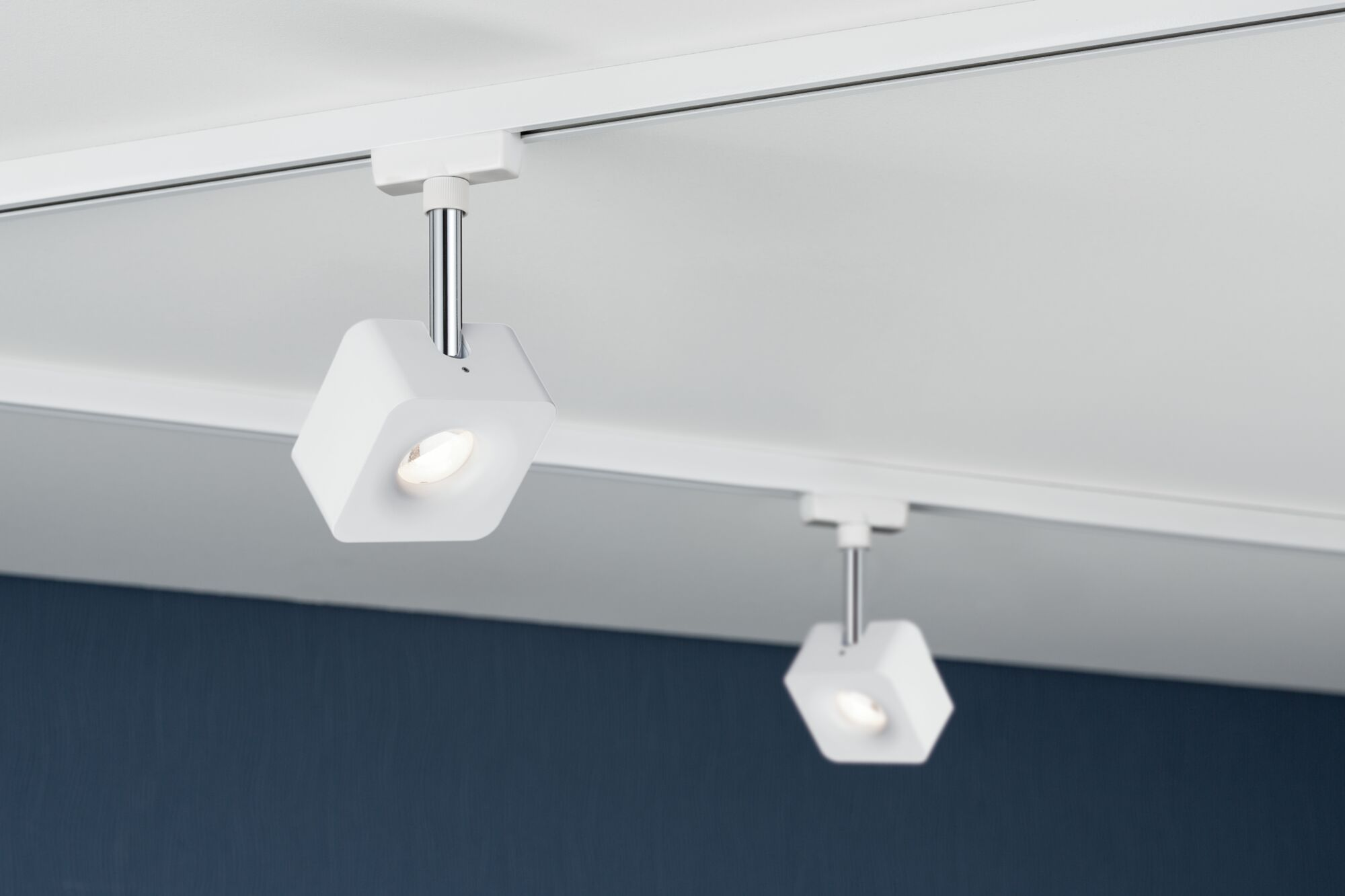 Zwei weiße Schienenstrahler mit sechseckigen Köpfen beleuchten eine Decke.
