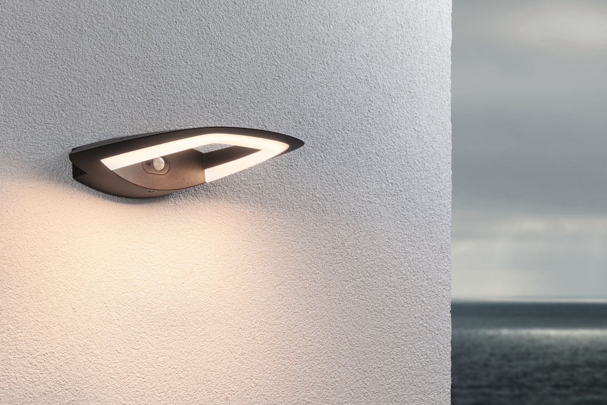 Nowoczesna ciemna lampa ścienna zewnętrzna z czujnikiem ruchu oświetla ścianę.